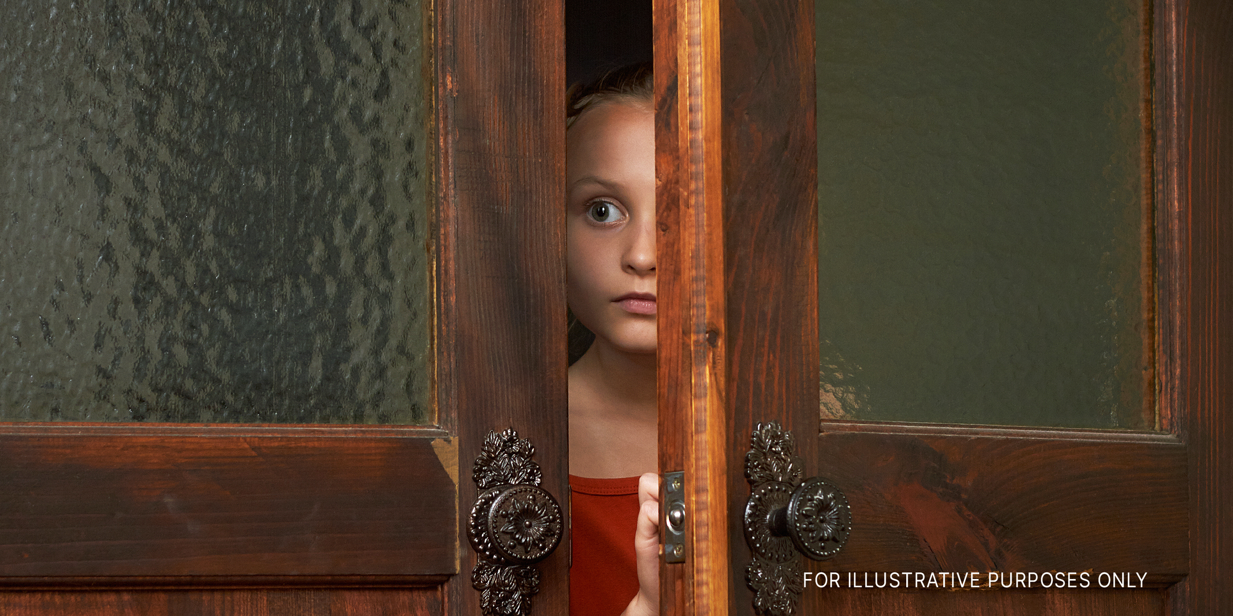 Ein kleines verängstigtes Mädchen schaut durch den Türschlitz | Quelle: Shutterstock