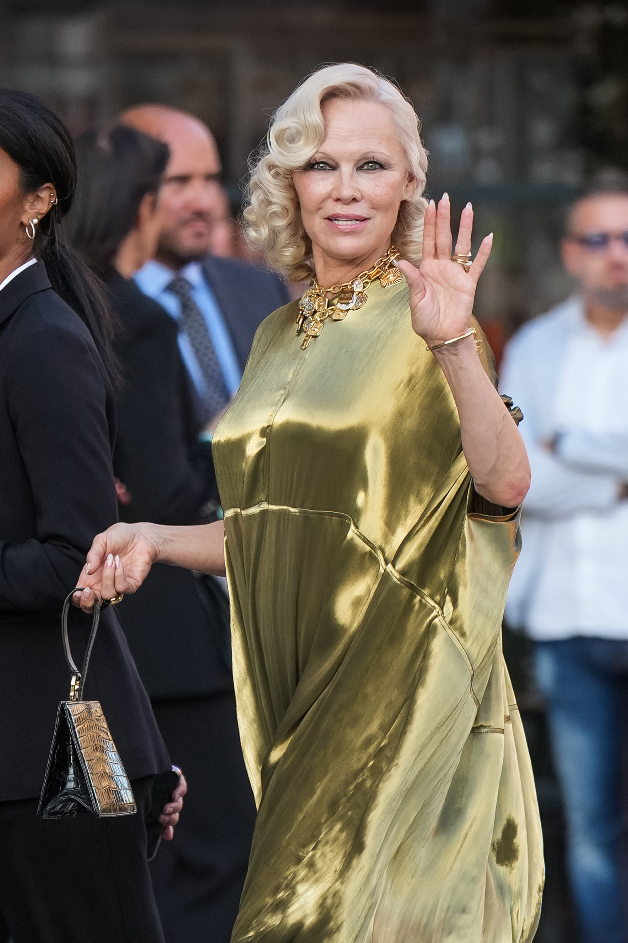 Ein genauerer Blick auf Anderson zeigt ihre platinblonden Locken, ihre auffällige goldene Halskette und ihr dunkles Augen-Make-up, während sie den Zuschauern in Mailand zuwinkt. Die Schauspielerin wurde am 22. September 2026 bei ihrer Ankunft während der Mailänder Modewoche fotografiert. | Quelle: Getty Images