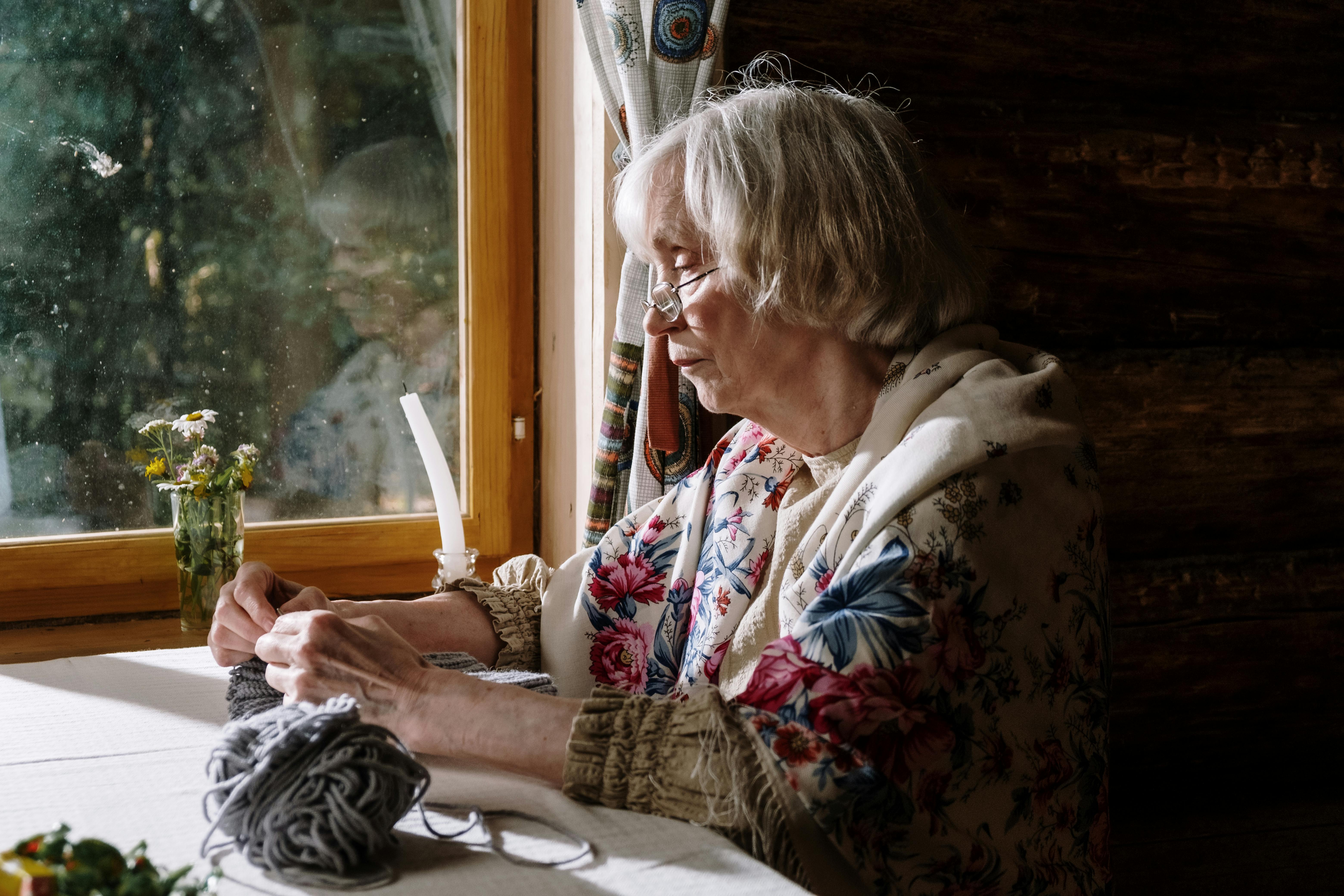 Oma strickt am Fenster, stolz und zufrieden | Quelle: Pexels