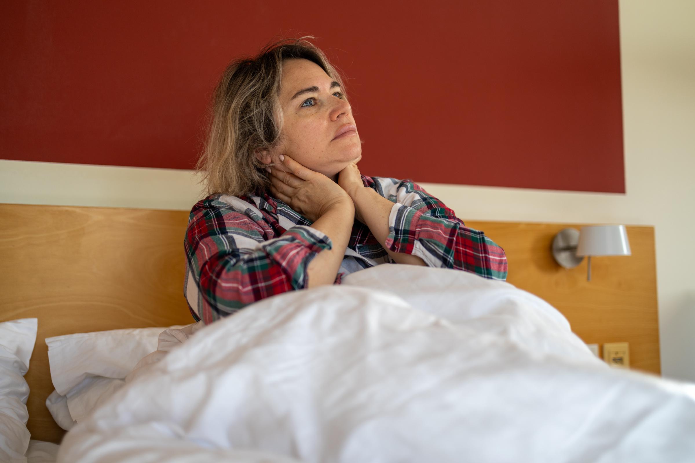Müde Frau, die im Bett sitzt und sich vor Schmerzen den Nacken hält, als Symbol für Stress, Burnout und psychische Probleme | Quelle: Getty Images