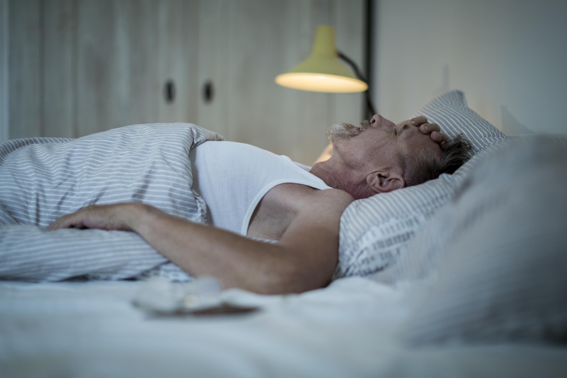 Mann liegt nachts wach im Bett, fühlt sich unwohl und kann nicht schlafen | Quelle: Getty Images