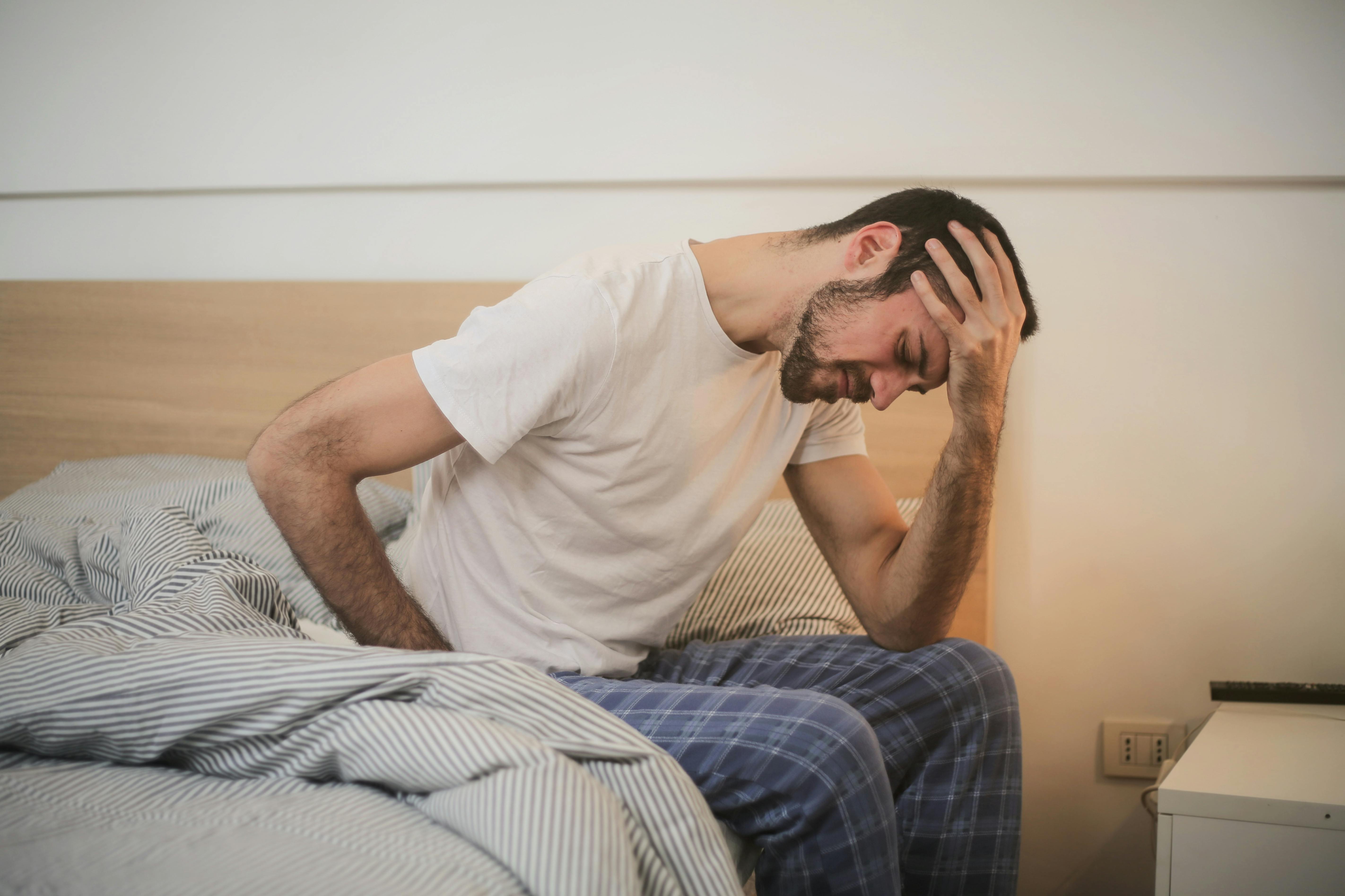 Ein aufgebrachter Mann hält sich den Kopf, während er auf einem Bett sitzt | Quelle: Pexels