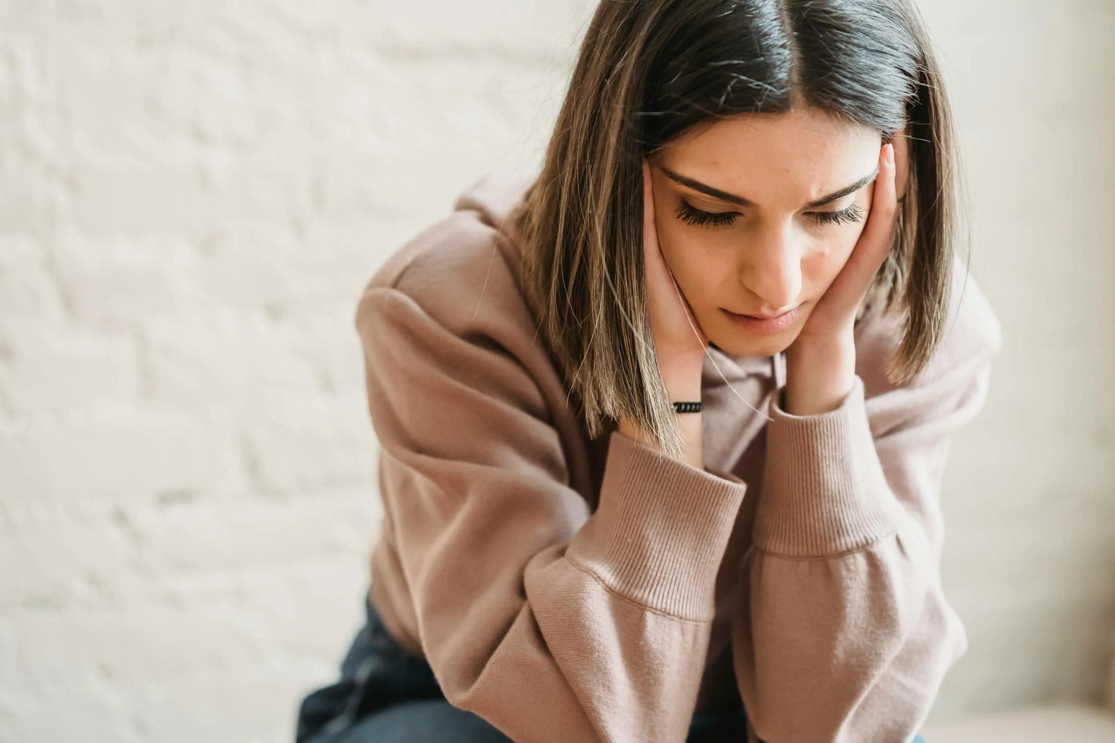 Uma mulher triste senta-se com os olhos fechados ⏐ Fonte: Pexels