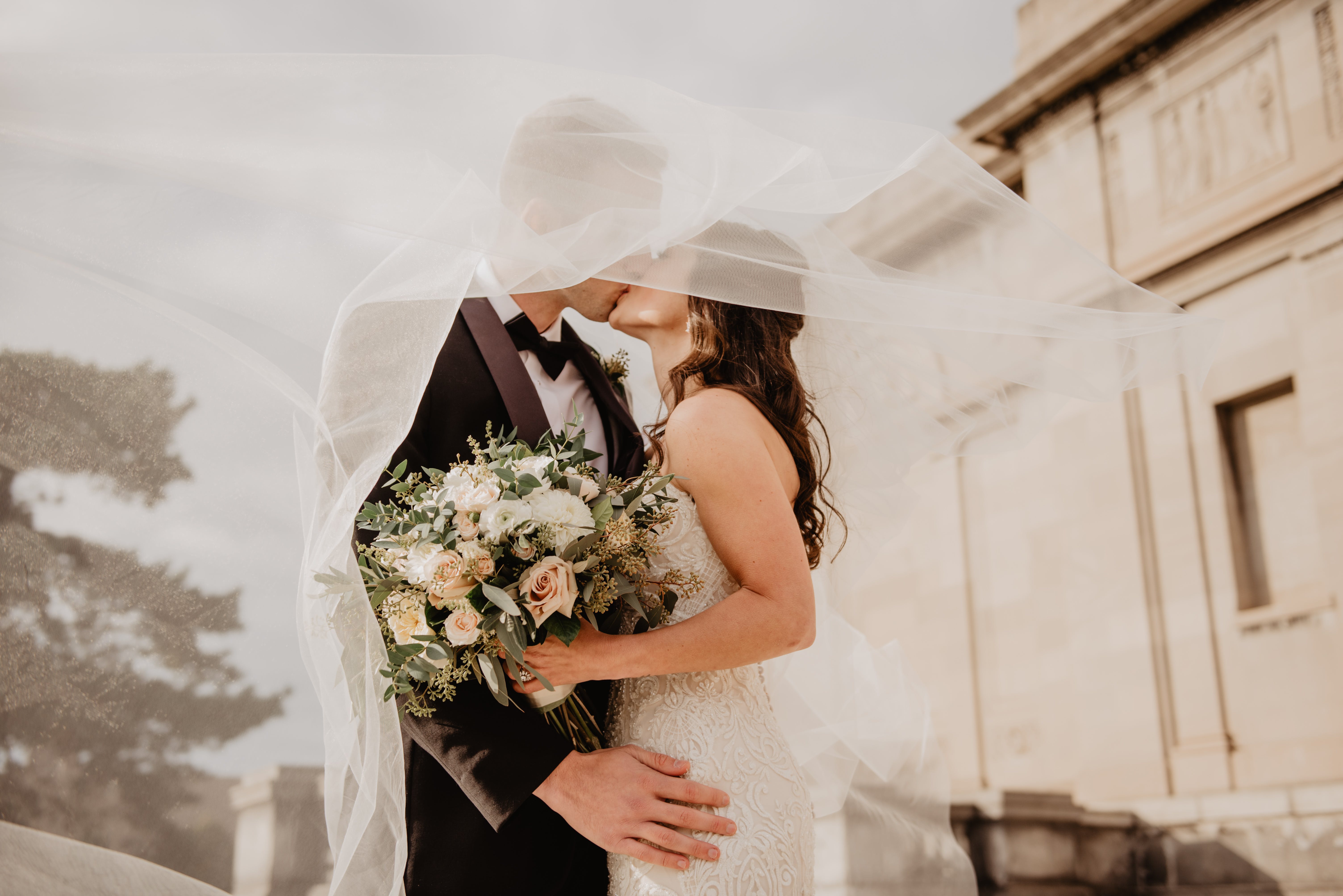 Ein frisch verheiratetes Paar küsst sich unter dem Schleier des Hochzeitskleides der Braut | Quelle: Pexels