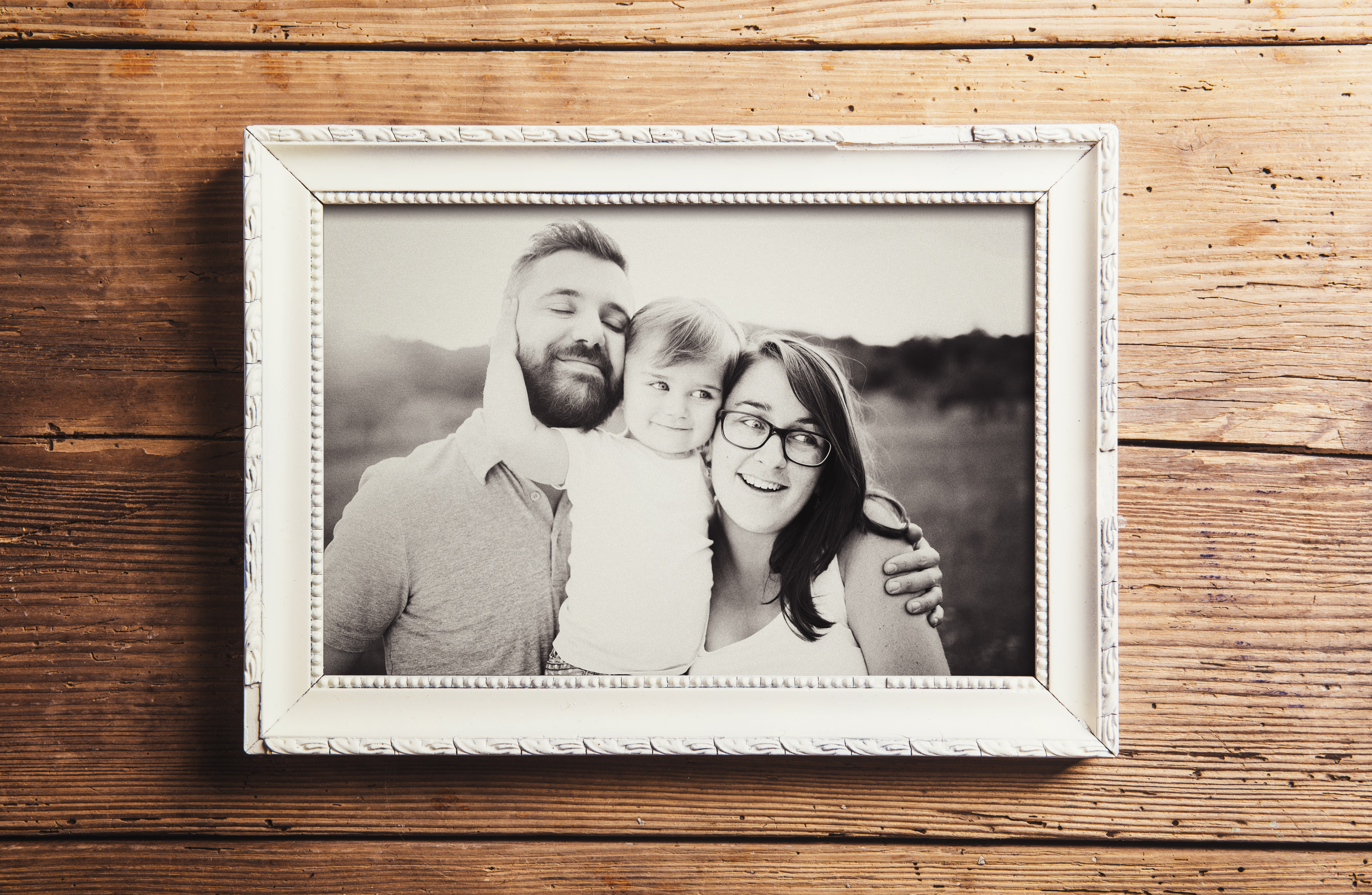 Ein Graustufenfoto von einer dreiköpfigen Familie in einem Holzrahmen | Quelle: Shutterstock