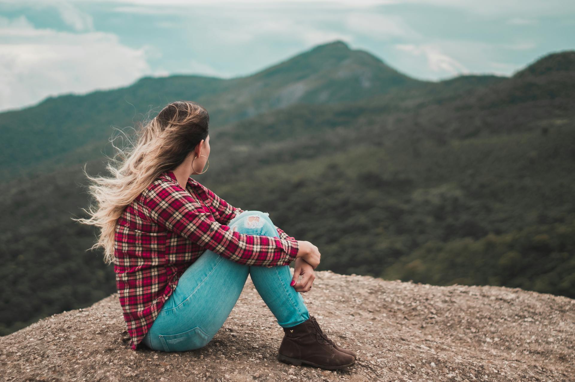 Eine Seitenansicht einer Frau, die auf dem Boden sitzt und einen Hügel überblickt | Quelle: Pexels