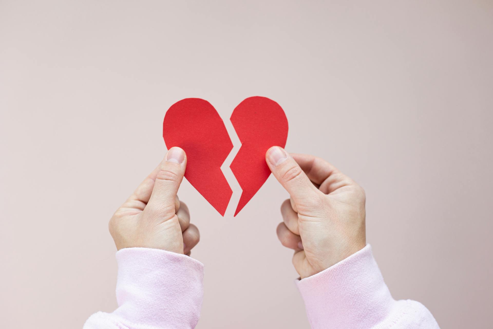 Eine Person, die ein zerbrochenes rotes Papierherz hält | Quelle: Pexels