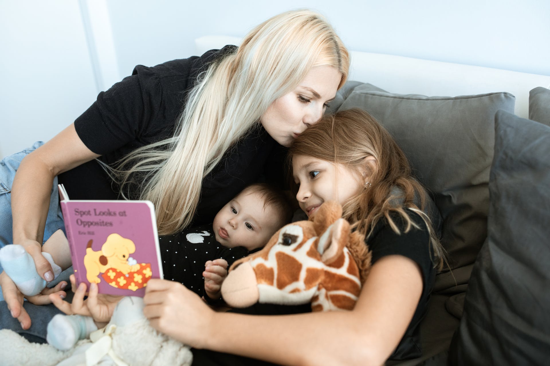 Eine Frau, die mit ihren beiden Kindern zusammen ist, indem sie ihnen ein Buch vorliest | Quelle: Pexels