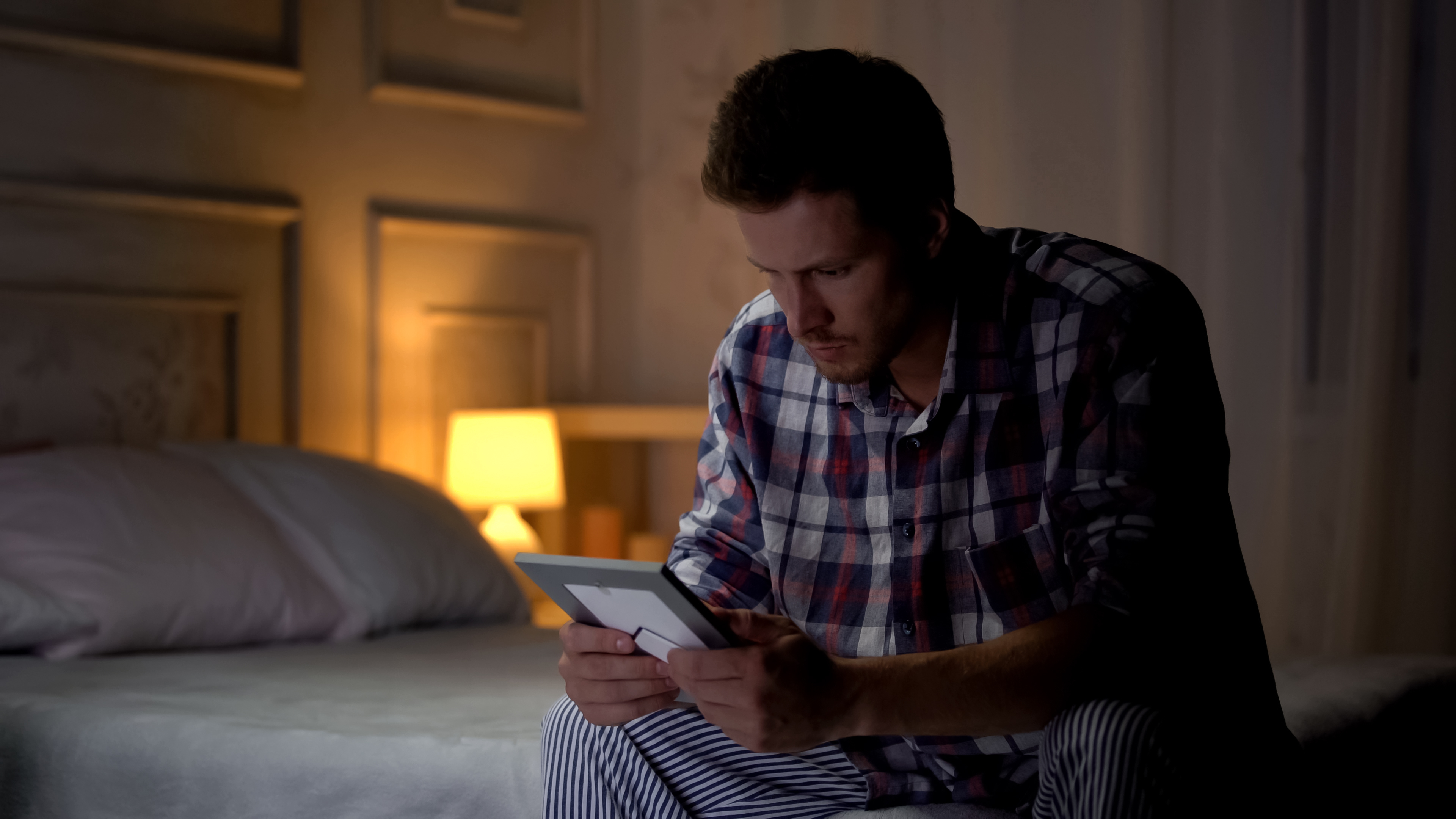 Ein unglücklicher Mann sitzt allein in seinem Zimmer und betrachtet ein Foto | Quelle: Shutterstock