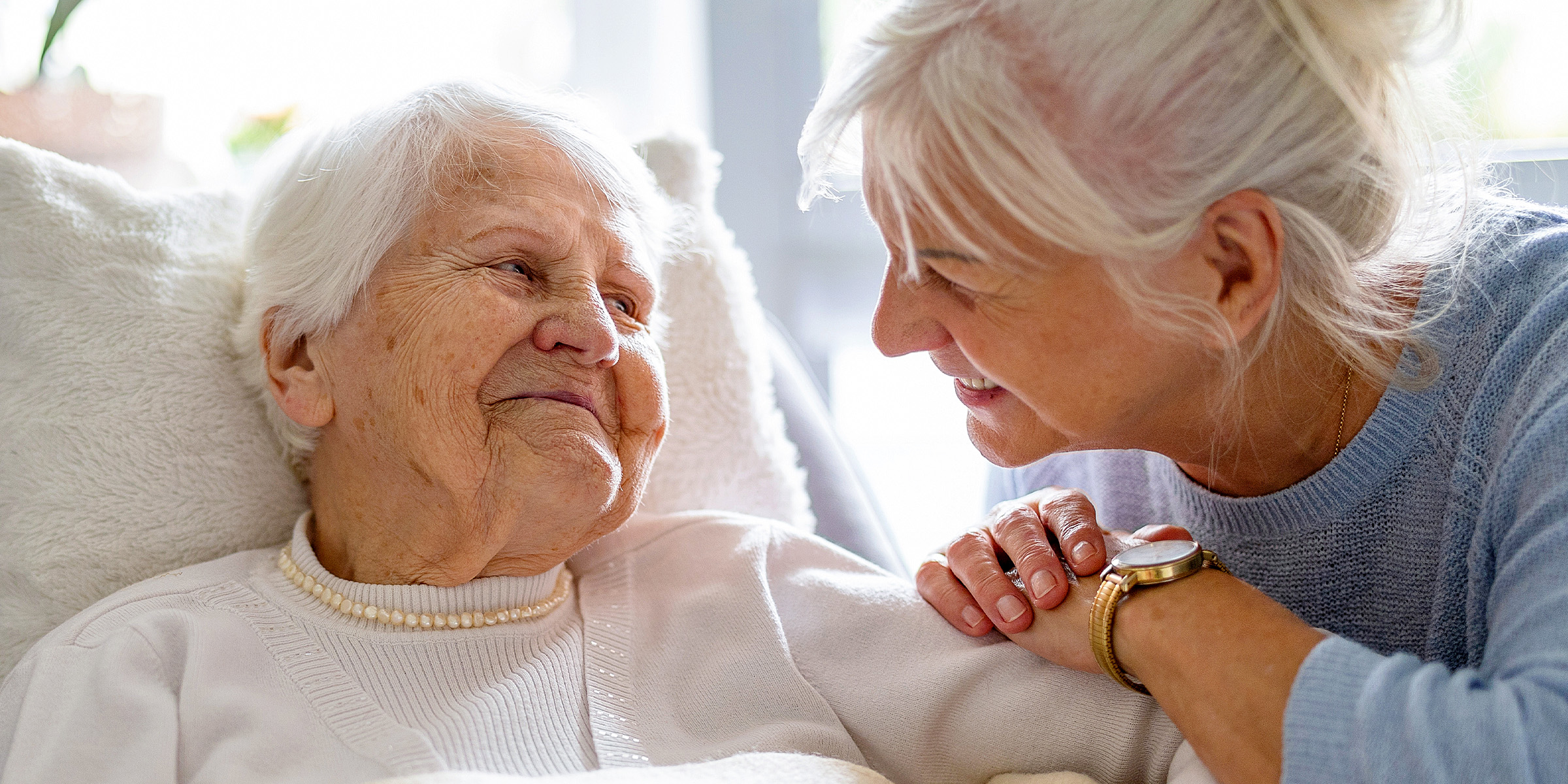 Eine jüngere Frau sitzt und spricht mit einer älteren Frau, die im Bett liegt | Quelle: Shutterstock