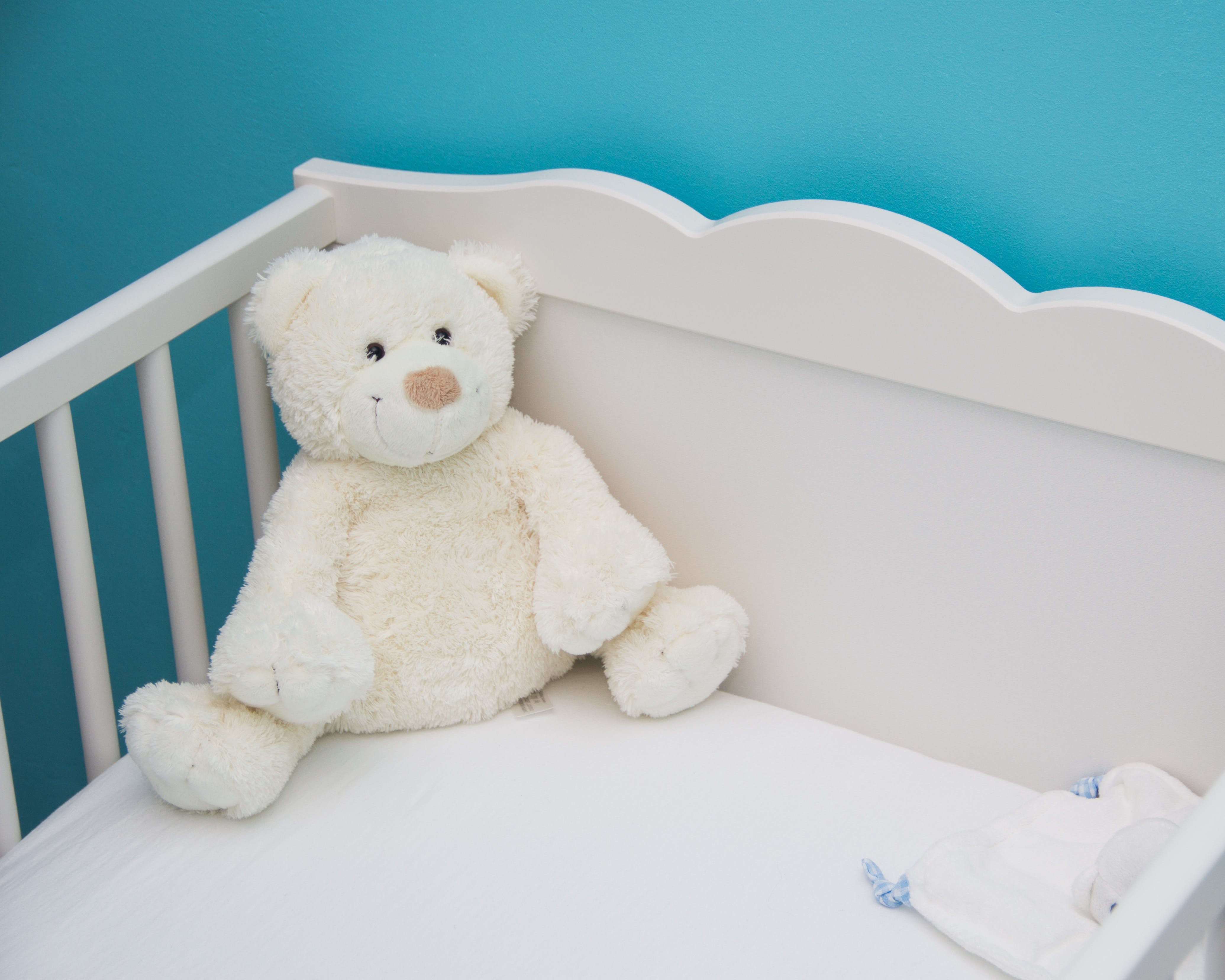 Ein weißes Teddybär-Spielzeug auf einem Babybett. | Quelle: Pexels