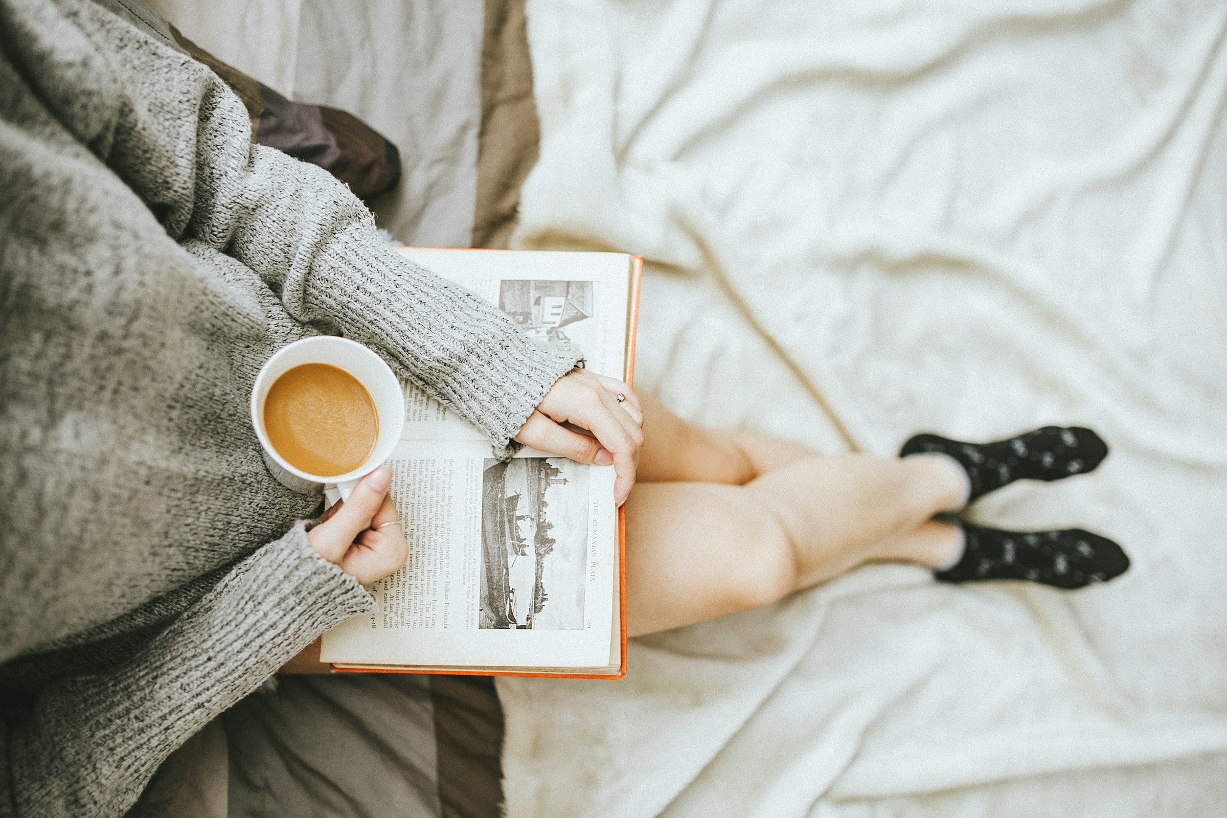 Eine Frau liest ein Buch, während sie zu Hause eine Tasse Kaffee genießt | Quelle: Unsplash