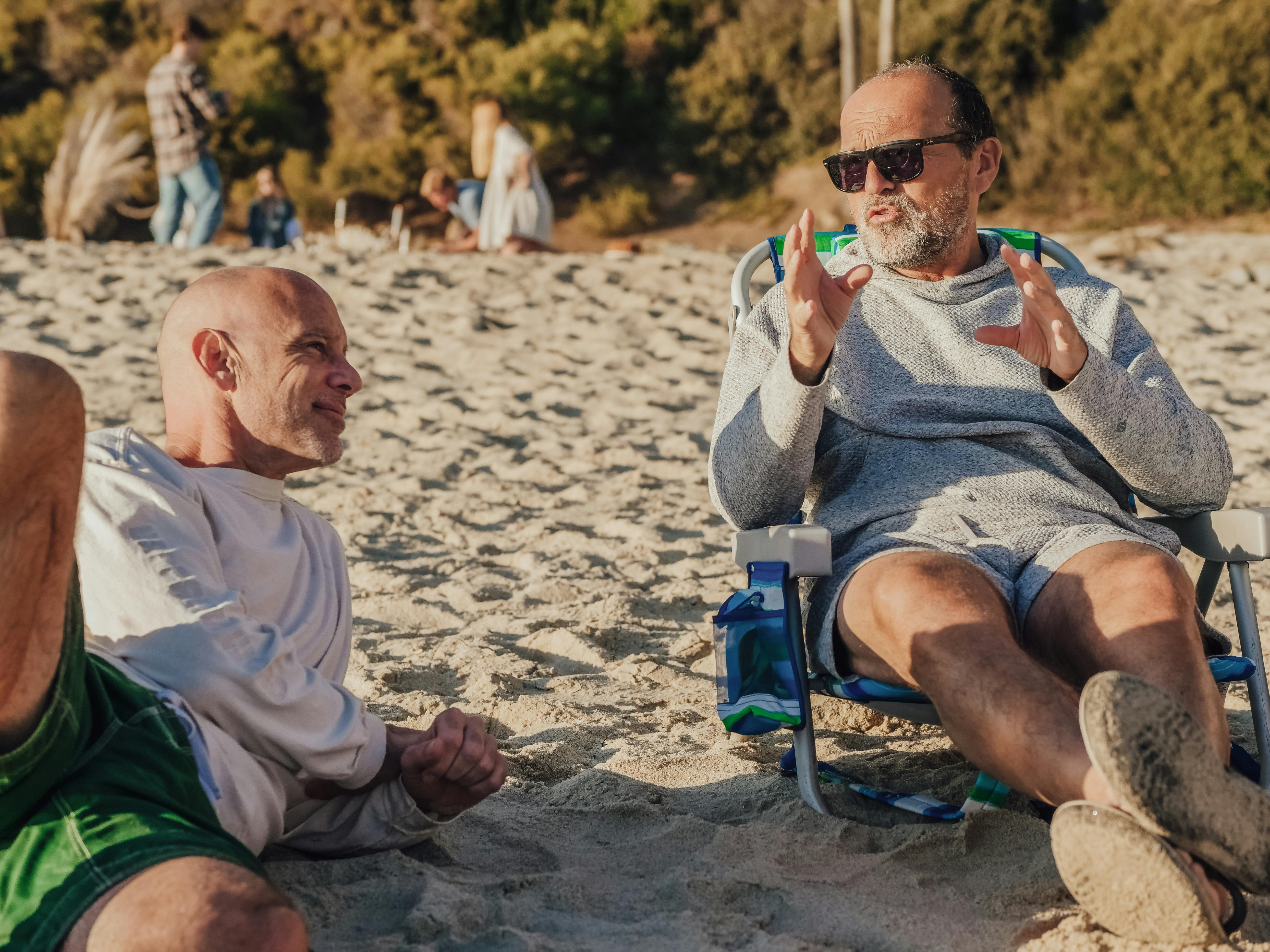 Ein Mann mittleren Alters, der am Strand vor einem anderen Mann mit etwas prahlt | Quelle: Pexels