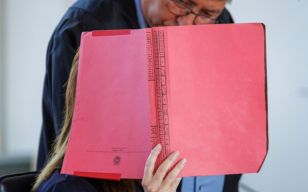 6. August 2026, Mecklenburg-Vorpommern, Rostock: Die Angeklagte sitzt bei der Eröffnung der Verhandlung vor dem Landgericht, bei der der Mordprozess im Fall Fabian wieder aufgenommen wird, neben ihrem Anwalt Andreas Ohm und hält sich eine Mappe vor das Gesicht. | Quelle: Getty Images