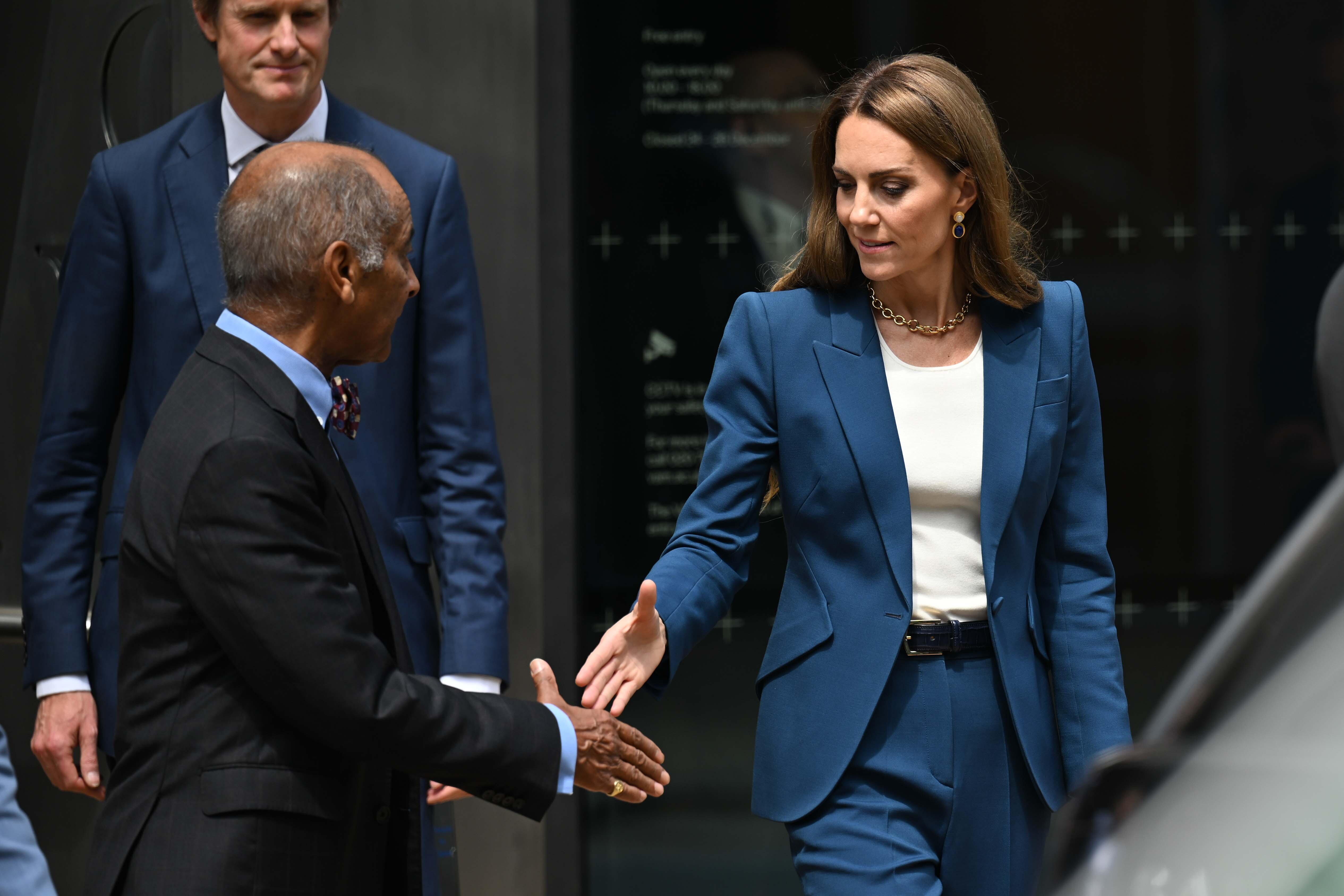 Mit ruhigem, konzentriertem Blick reicht Prinzessin Catherine die Hand zum Händedruck. Ihr maßgeschneiderter blauer Anzug und ihre ruhige Haltung vermitteln Eleganz und Aufmerksamkeit in einer formellen Umgebung.