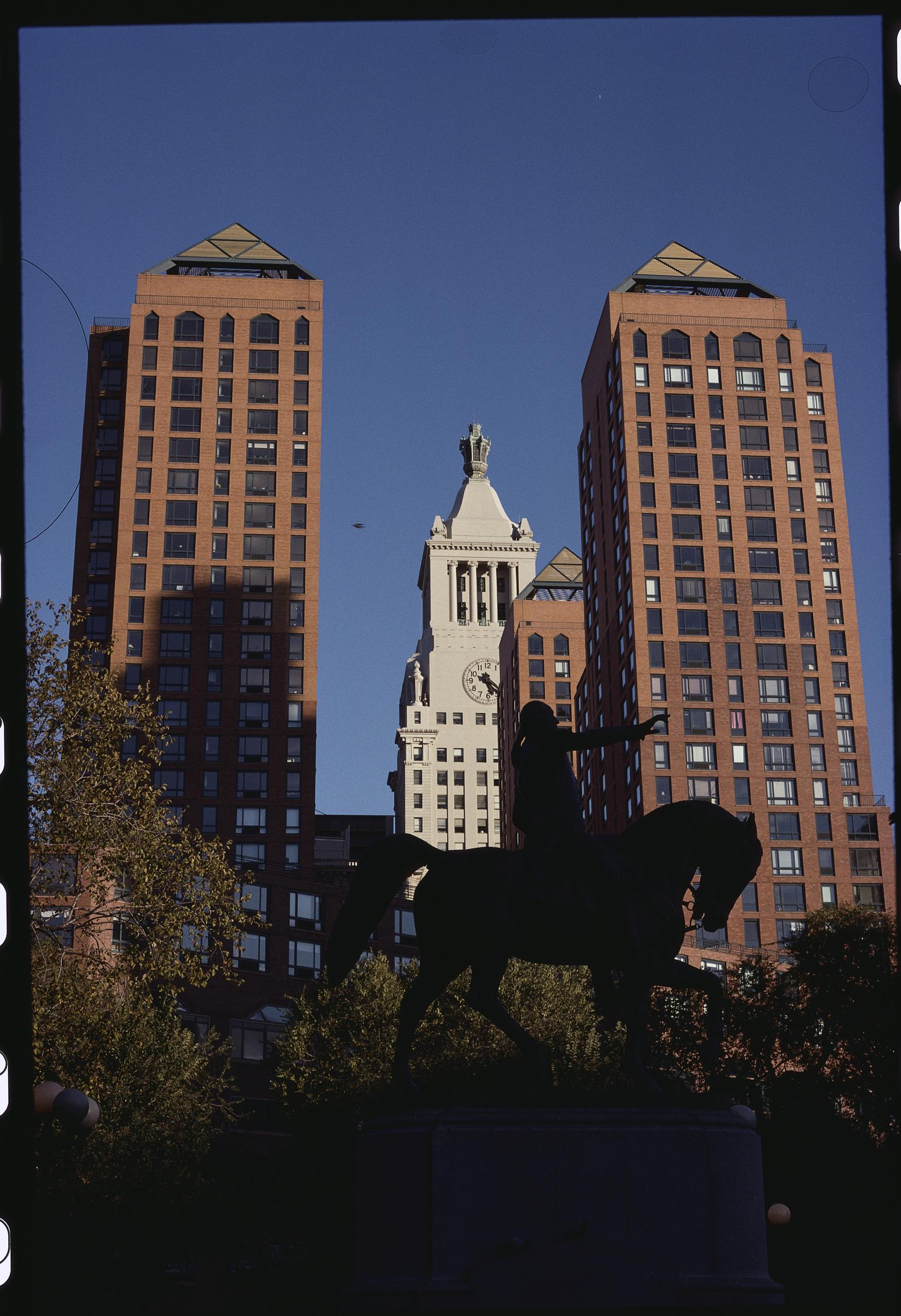 Die Hochhäuser der Zeckendorf Towers aus rotem Backstein flankieren den historischen Uhrturm von Consolidated Edison am Union Square Park, während sich im Vordergrund unter einem strahlend blauen Himmel die Silhouette der Reiterstatue von George Washington abzeichnet. | Quelle: Getty Images