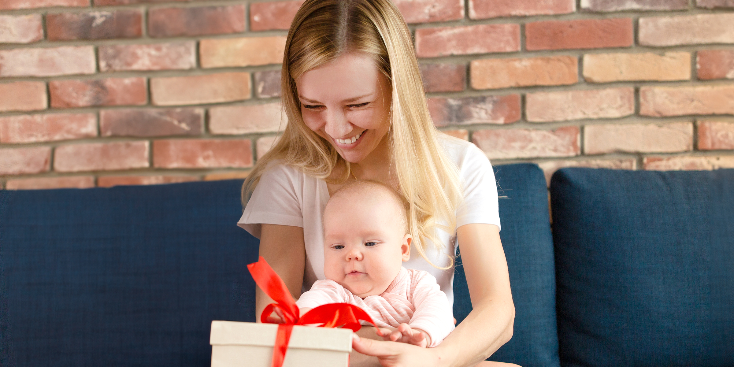 Eine lächelnde Frau, die ein Baby und eine Geschenkbox hält | Quelle: Shutterstock