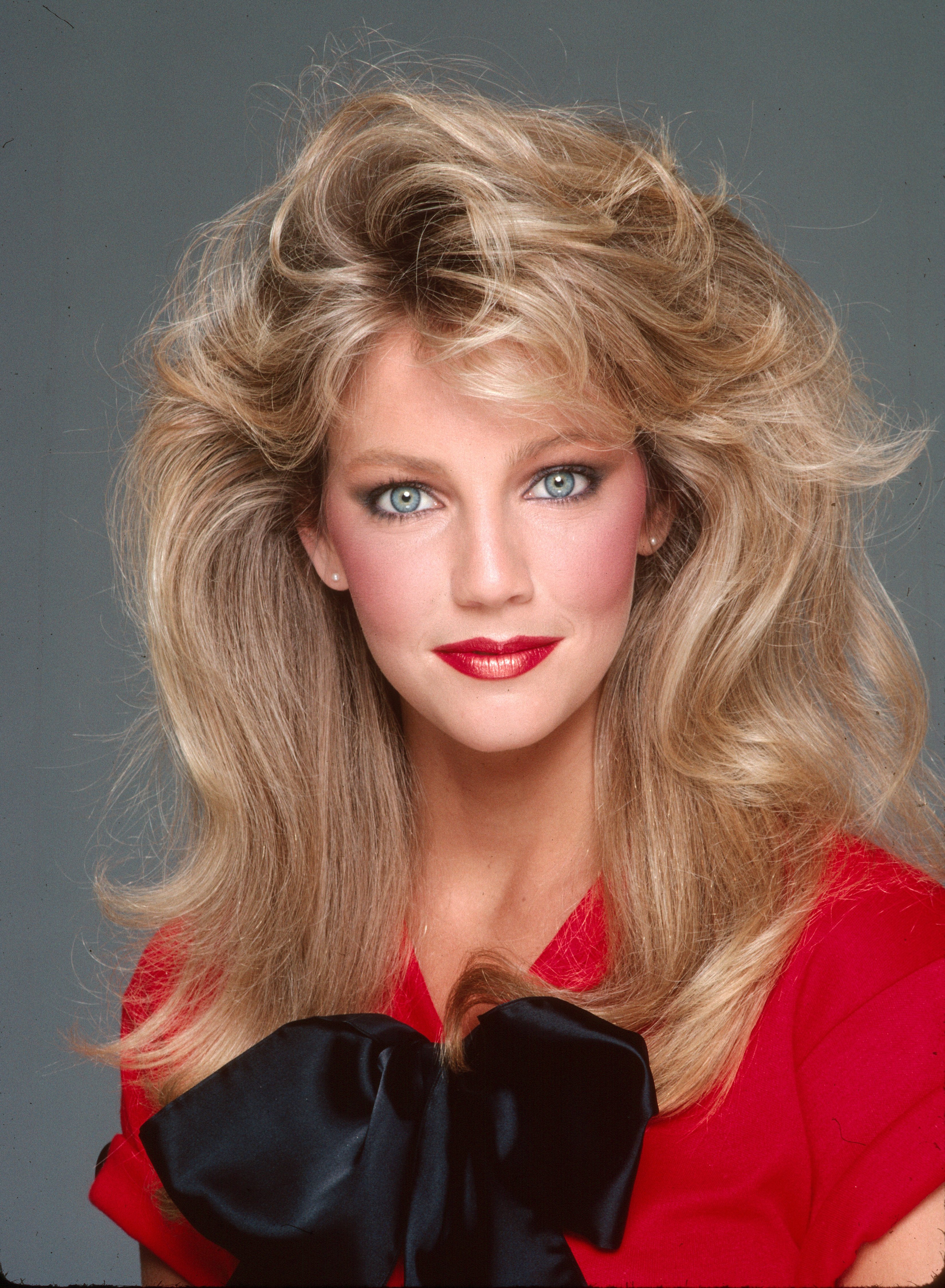 Heather Locklear verkörpert den Glamour der 1980er Jahre bei einem Studio-Fotoshooting am 2. Februar 1981 in Los Angeles, Kalifornien. Mit voluminösen, gestuften blonden Locken, die ihr Gesicht umrahmen, blickt sie direkt in die Kamera und präsentiert dabei rosiges Rouge, knallroten Lippenstift und Perlenohrstecker, während sie ein leuchtend rotes Oberteil trägt, das mit einer übergroßen schwarzen Satinschleife akzentuiert ist. | Quelle: Getty Images