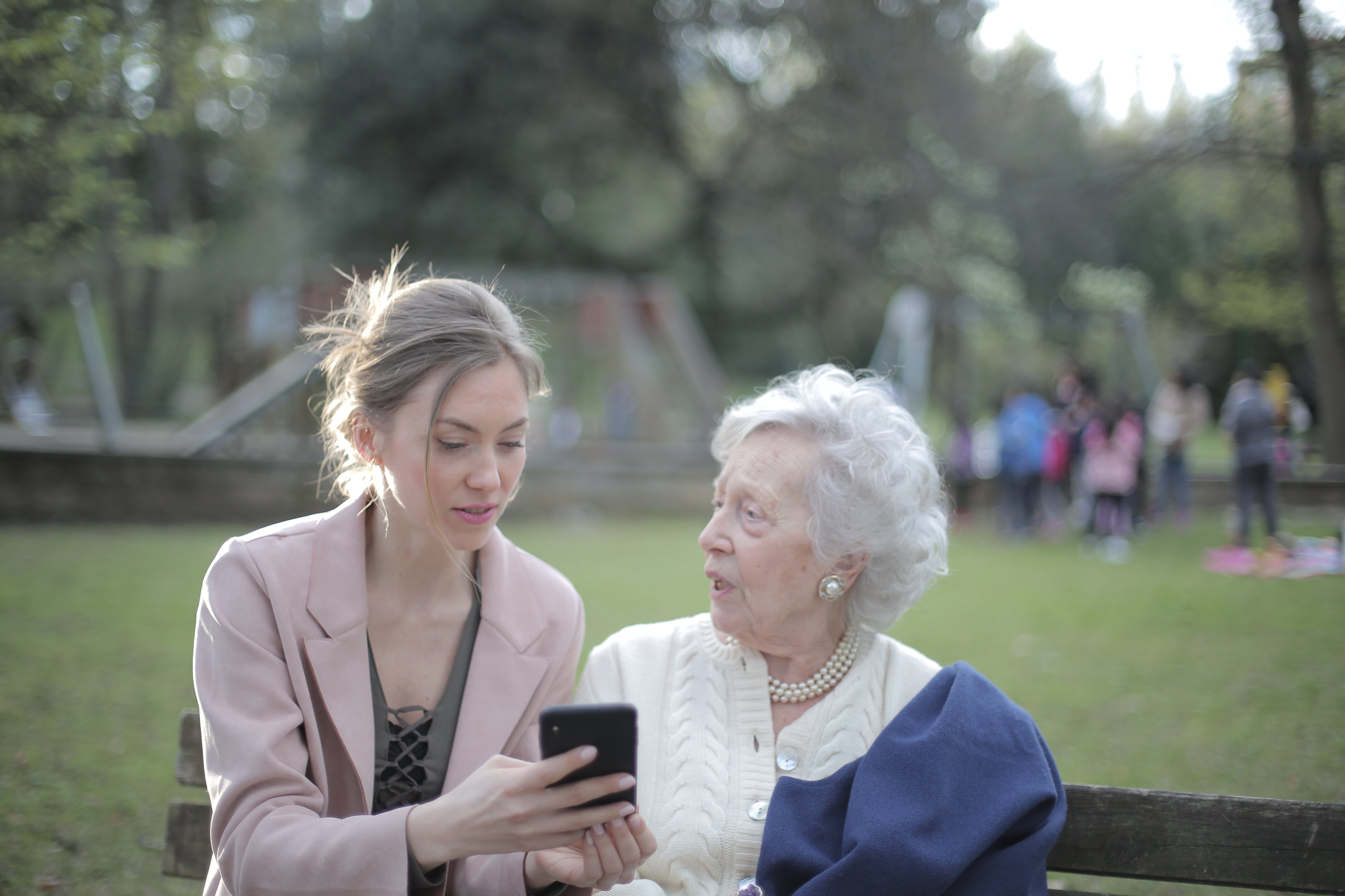 Eine jüngere Frau zeigt einer älteren etwas auf ihrem Handy, während sie draußen ist | Quelle: Pexels