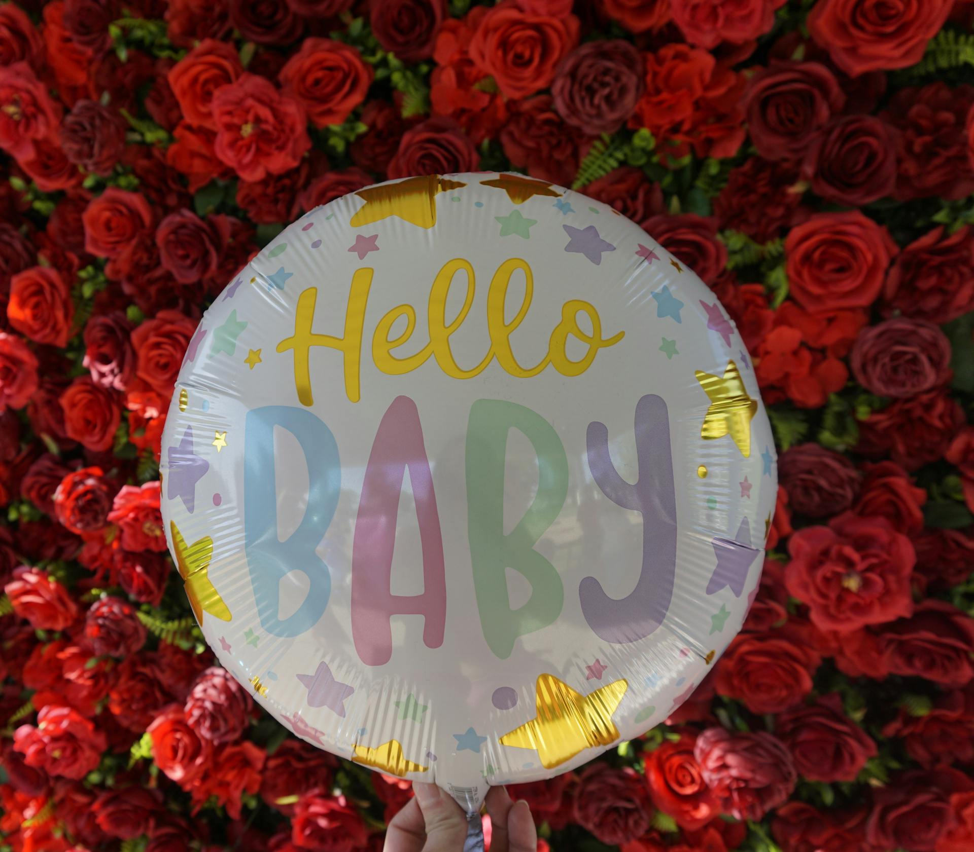 Eine Person hält einen Luftballon mit roten Rosen im Hintergrund | Quelle: Pexels