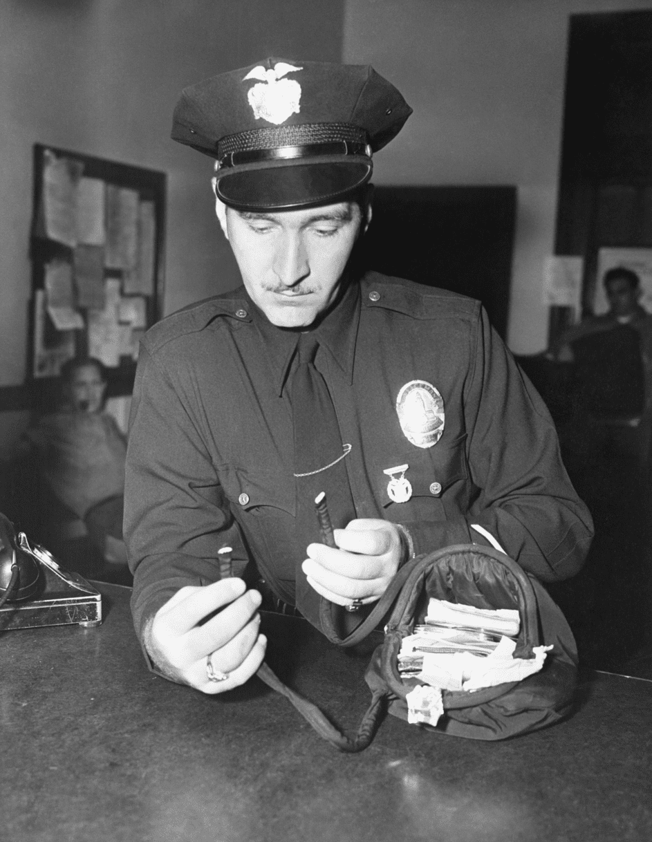 Polizisr Howard Rose hält Jean Spanglers beschädigte Handtasche, ein Beweismittel. 1949 | Quelle: Getty Images