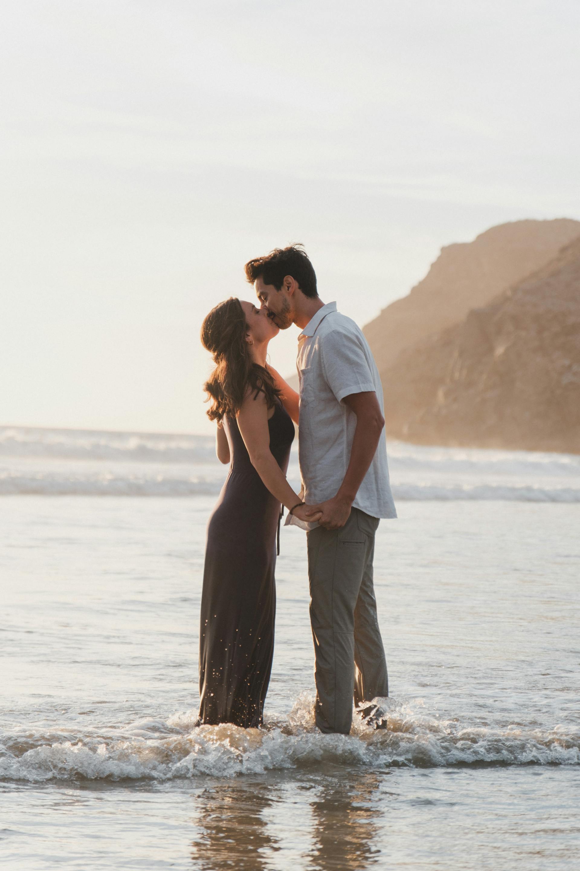 Ein Paar, das sich küsst, während es knöcheltief im Meer steht | Quelle: Pexels