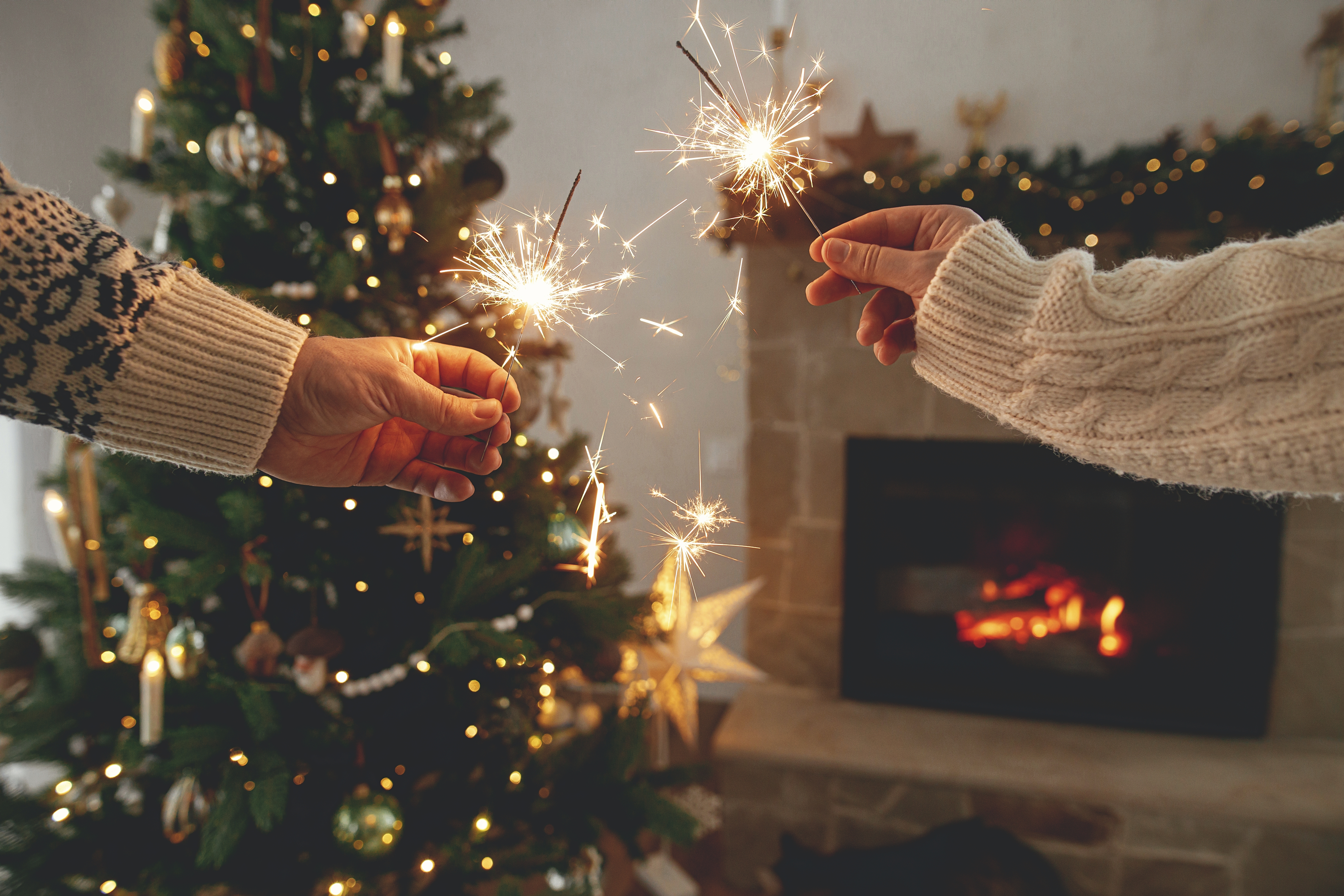 Zwei Menschen zünden Wunderkerzen in der Nähe eines Weihnachtsbaums an | Quelle: Shutterstock