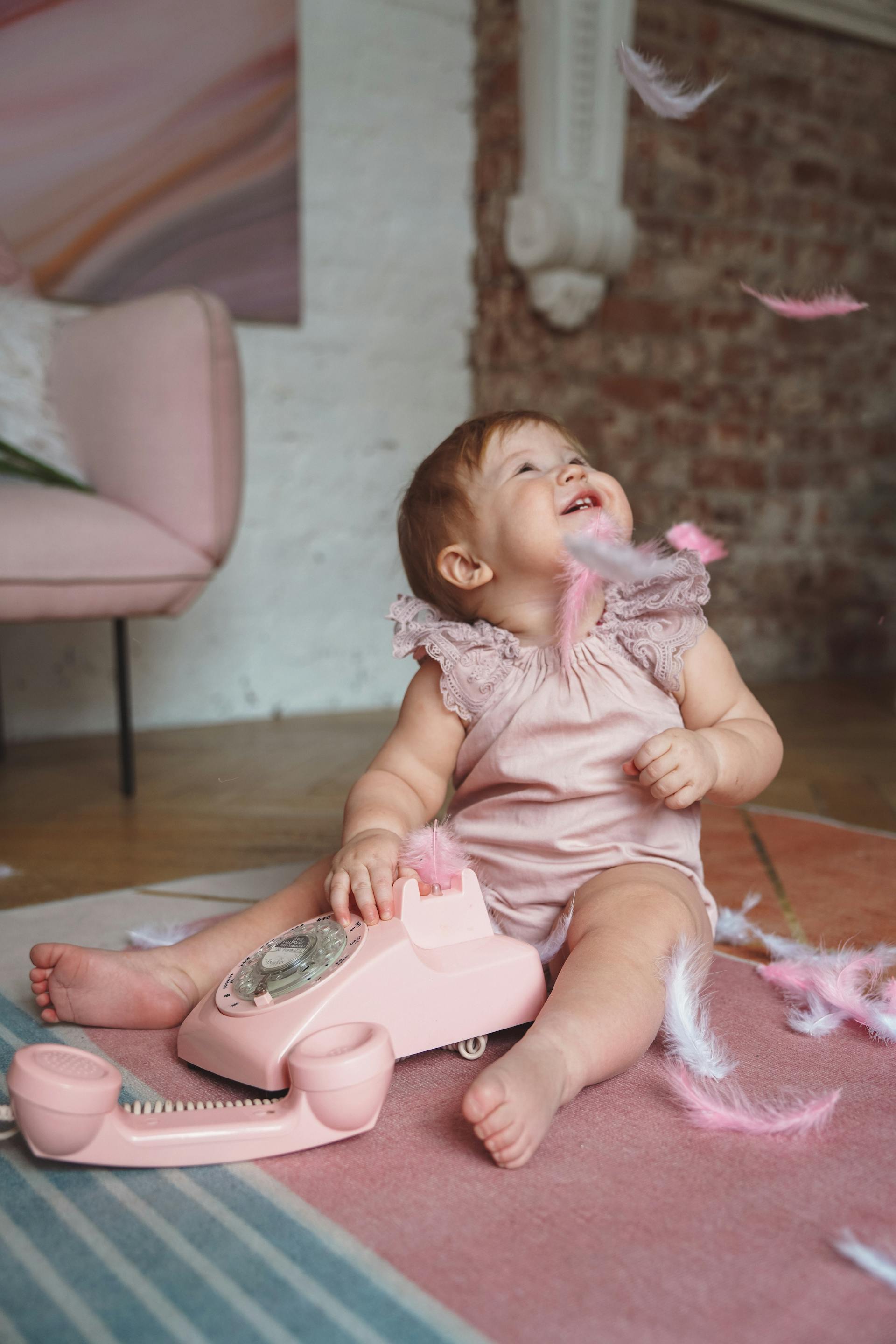 Ein kleines Mädchen in rosa Kleidung spielt mit Federn und einem rosa Telefon