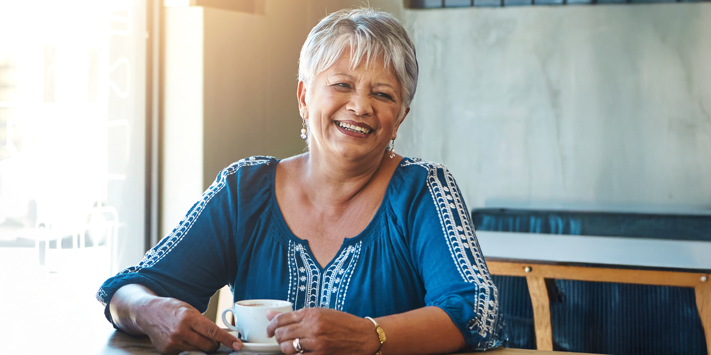 Eine erfreute ältere Frau mit kurzen grauen Haaren sitzt an einem Tisch | Quelle: Shutterstock