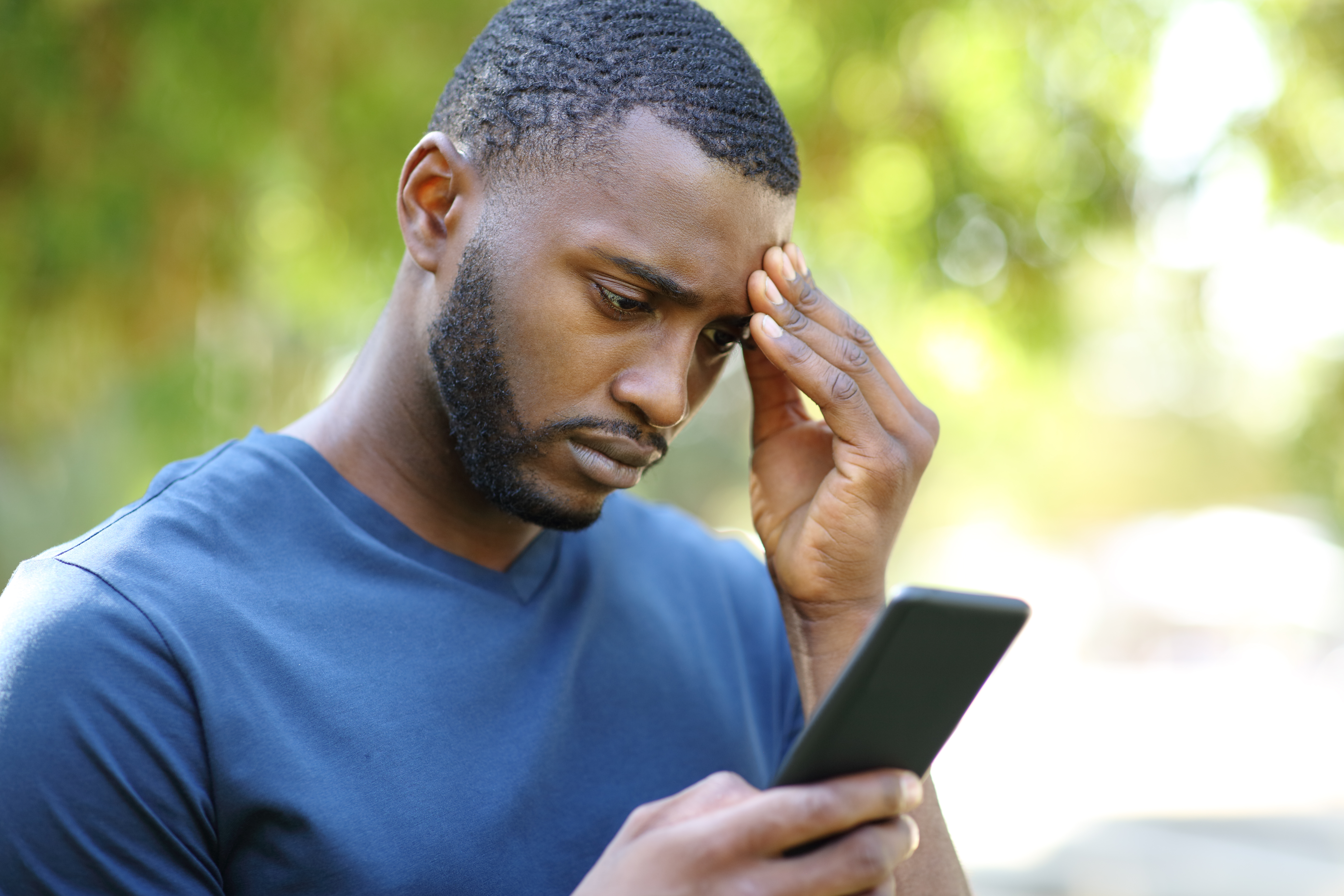 Besorgter schwarzer Mann überprüft sein Smartphone in einem Park | Quelle: Getty Images