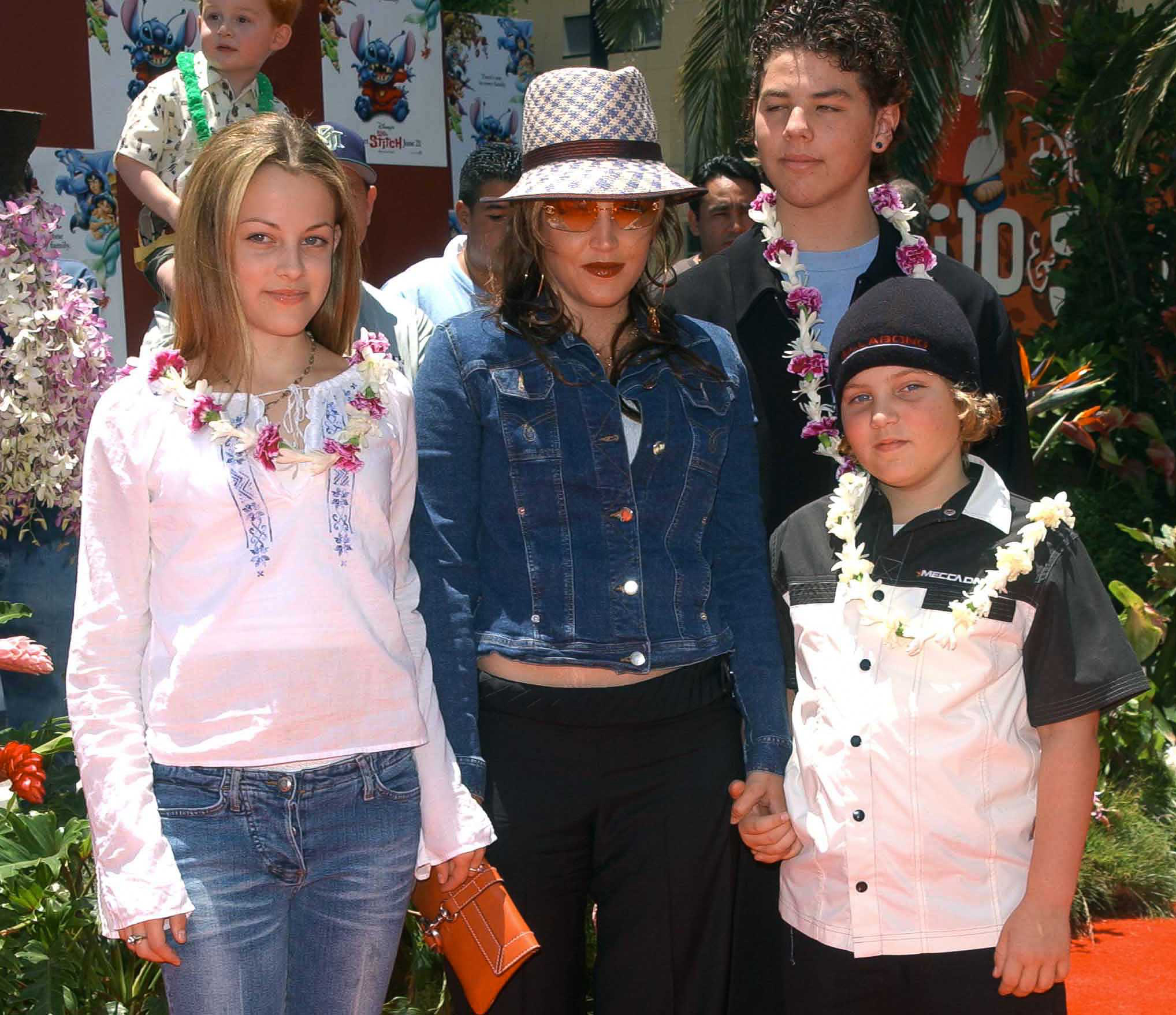 Lisa Marie Presley posiert mit ihren Kindern Riley Keough und Benjamin Keough sowie ihrem Halbbruder Navarone Garibaldi bei der Premiere von „Lilo & Stitch“ im El Capitan Theatre in Hollywood, Kalifornien, am 16. Juni 2002. Presley trägt eine Jeansjacke, eine getönte Sonnenbrille und einen gemusterten Fedora, während die Familie auf dem roten Teppich hawaiianische Lei-Ketten trägt. | Quelle: Getty Images