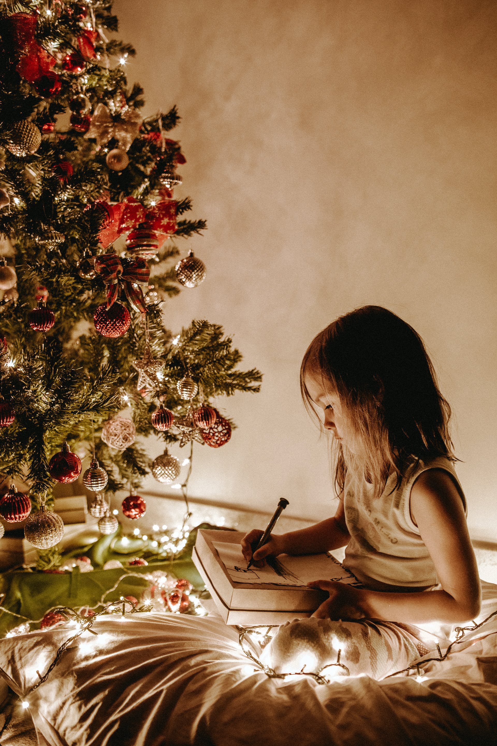 Ein kleines Mädchen sitzt neben einem Weihnachtsbaum | Quelle: Pexels