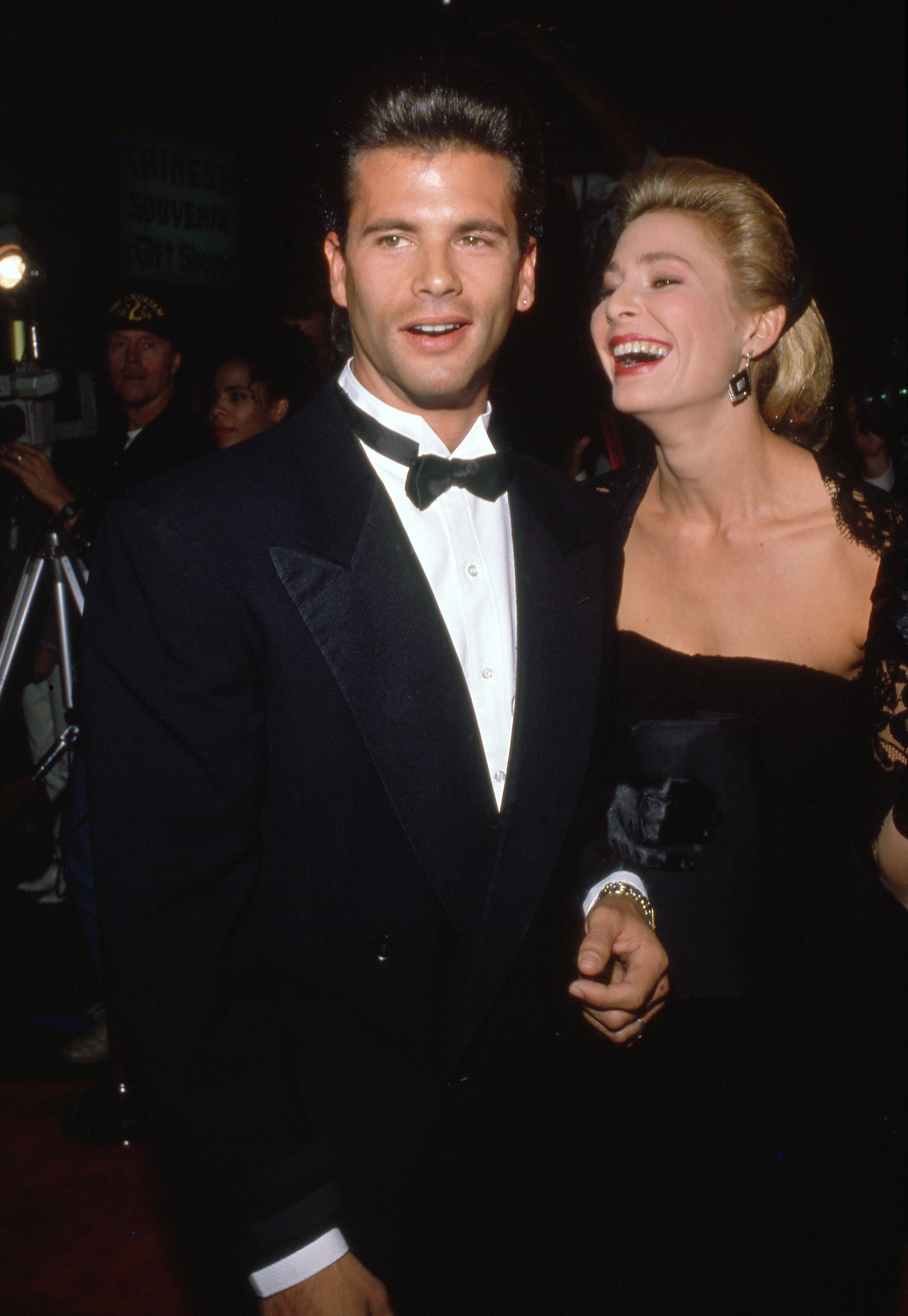 Lorenzo Lamas und seine damalige Frau, die Schauspielerin Kathleen Kinmont, genießen einen fröhlichen Moment auf dem roten Teppich bei einer Abendveranstaltung in den 1990er Jahren. Lamas sieht in einem klassischen schwarzen Smoking, einem weißen Plisseehemd und einer schwarzen Fliege schick aus, während Kinmont neben ihm in einem eleganten schwarzen Kleid, mit nach hinten gekämmten blonden Haaren und auffälligen Ohrringen lacht. | Quelle: Getty Images