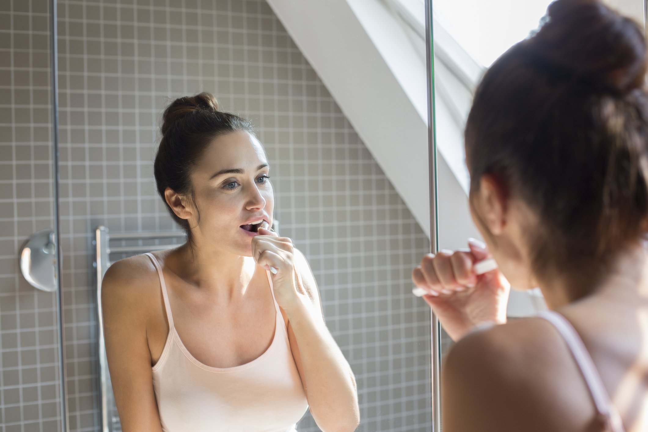 Frau, die Zähne im Badezimmerspiegel putzt. I Foto: Getty Images