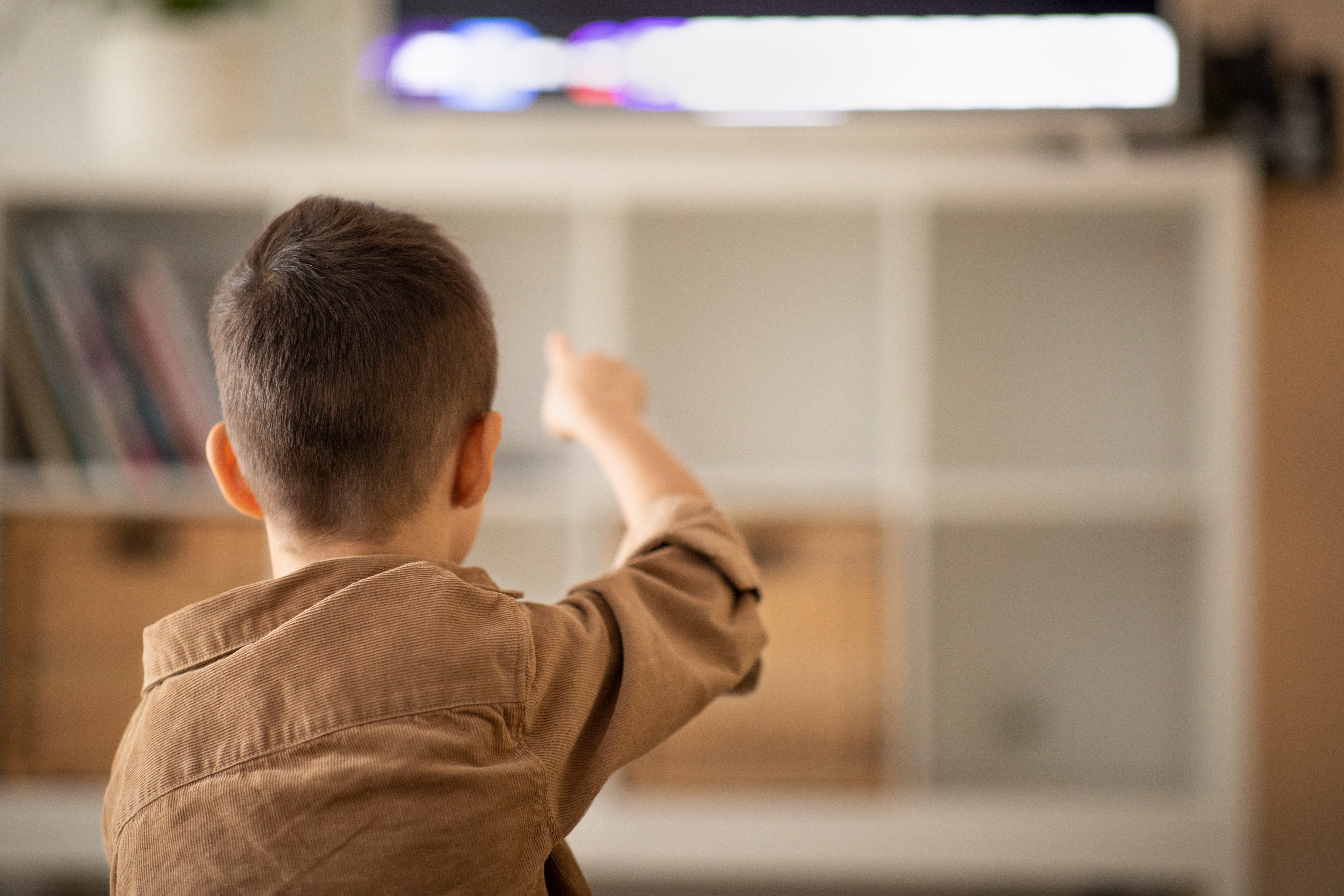 Ein kleiner Junge sieht sich ein Video an und zeigt mit dem Finger auf den Fernseher | Quelle: Shutterstock
