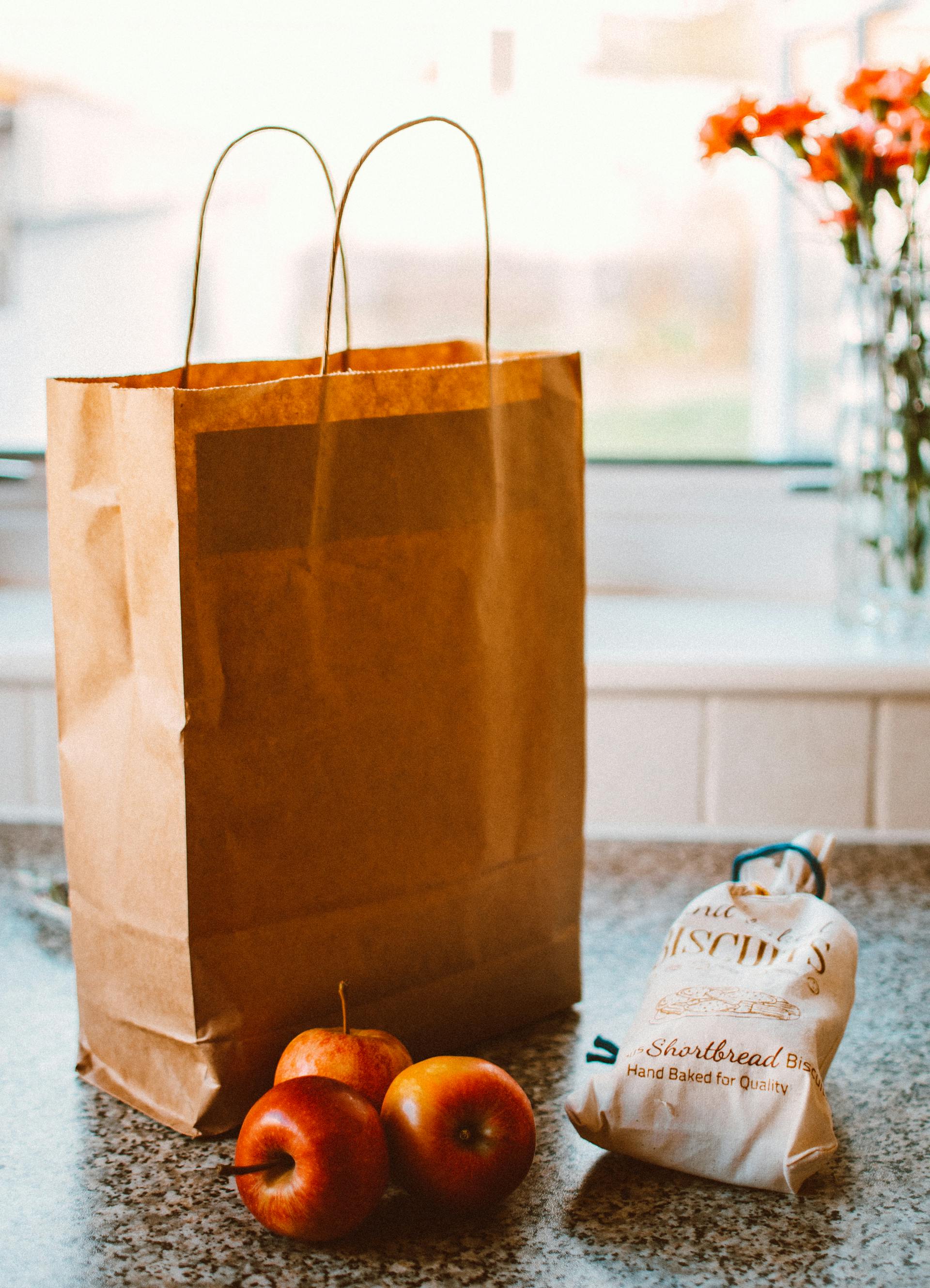 Mehrere Äpfel liegen neben einer braunen Papiertüte und einer Packung Brot | Quelle: Pexels