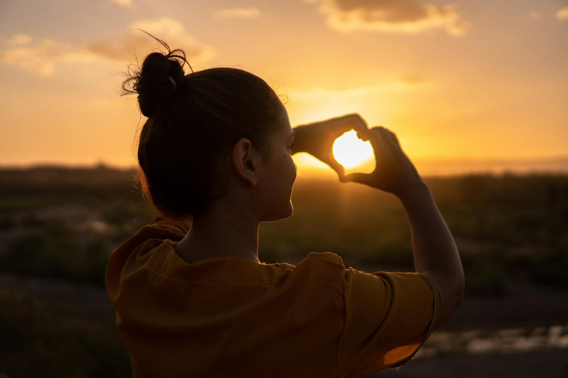 Eine Rückansicht einer Frau, die während der goldenen Stunde ein Herzzeichen mit ihren Händen macht | Quelle: Pexels