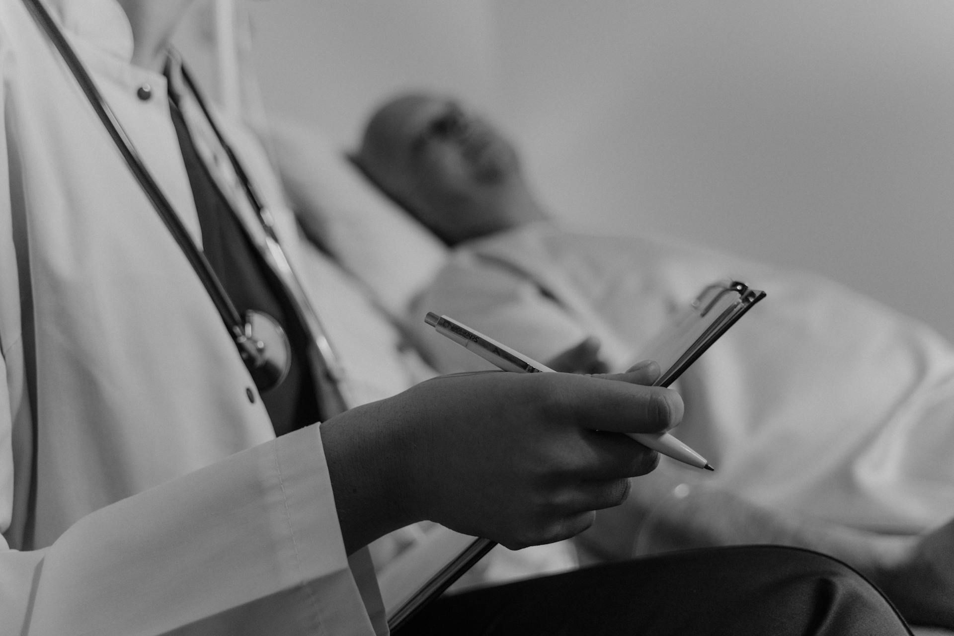 Ein Graustufenfoto eines Arztes, der eine Krankenakte hält und neben einem Patienten steht | Quelle: Pexels