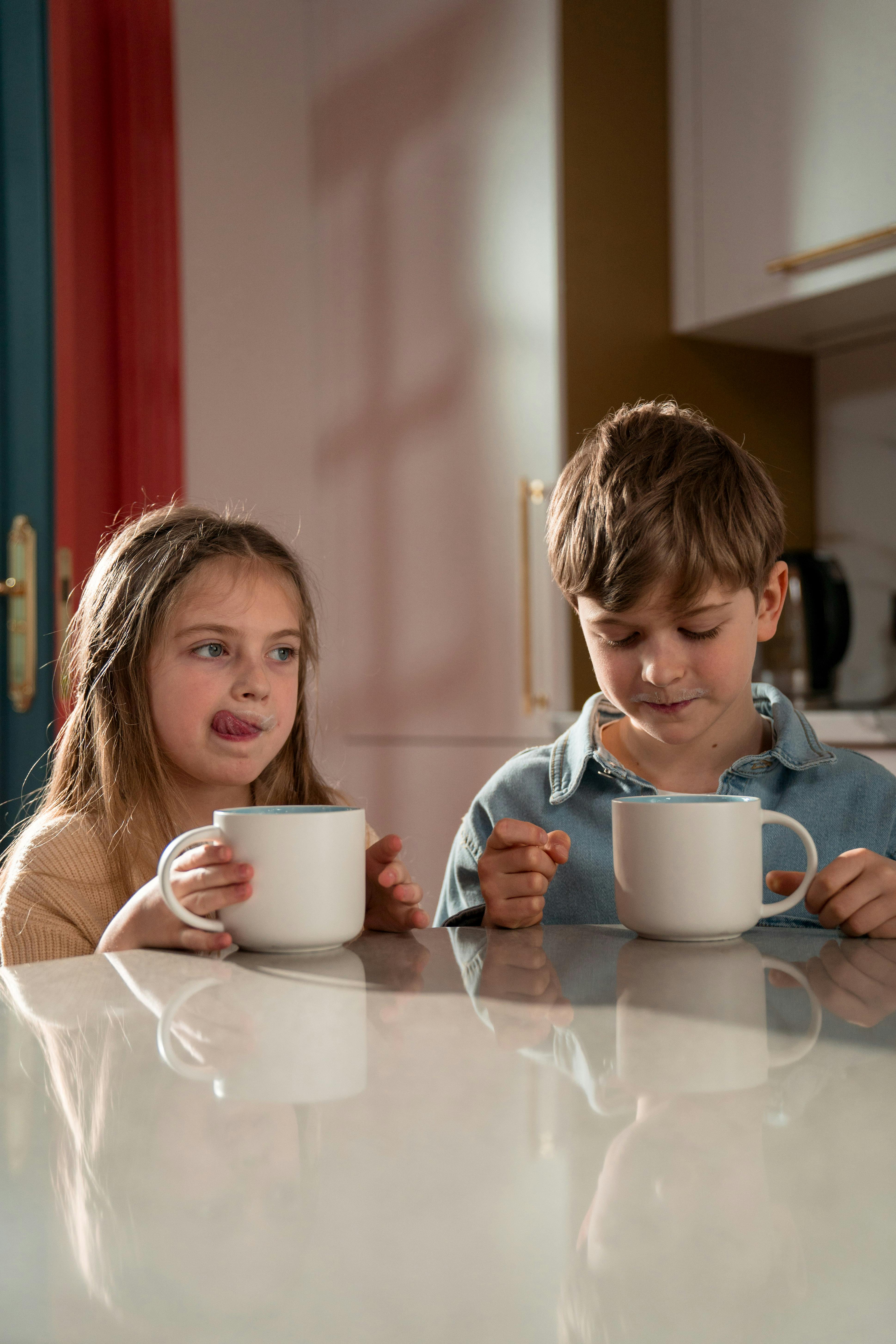 Zwei Kinder sitzen am Tisch und genießen ihre Getränke | Quelle: Pexels