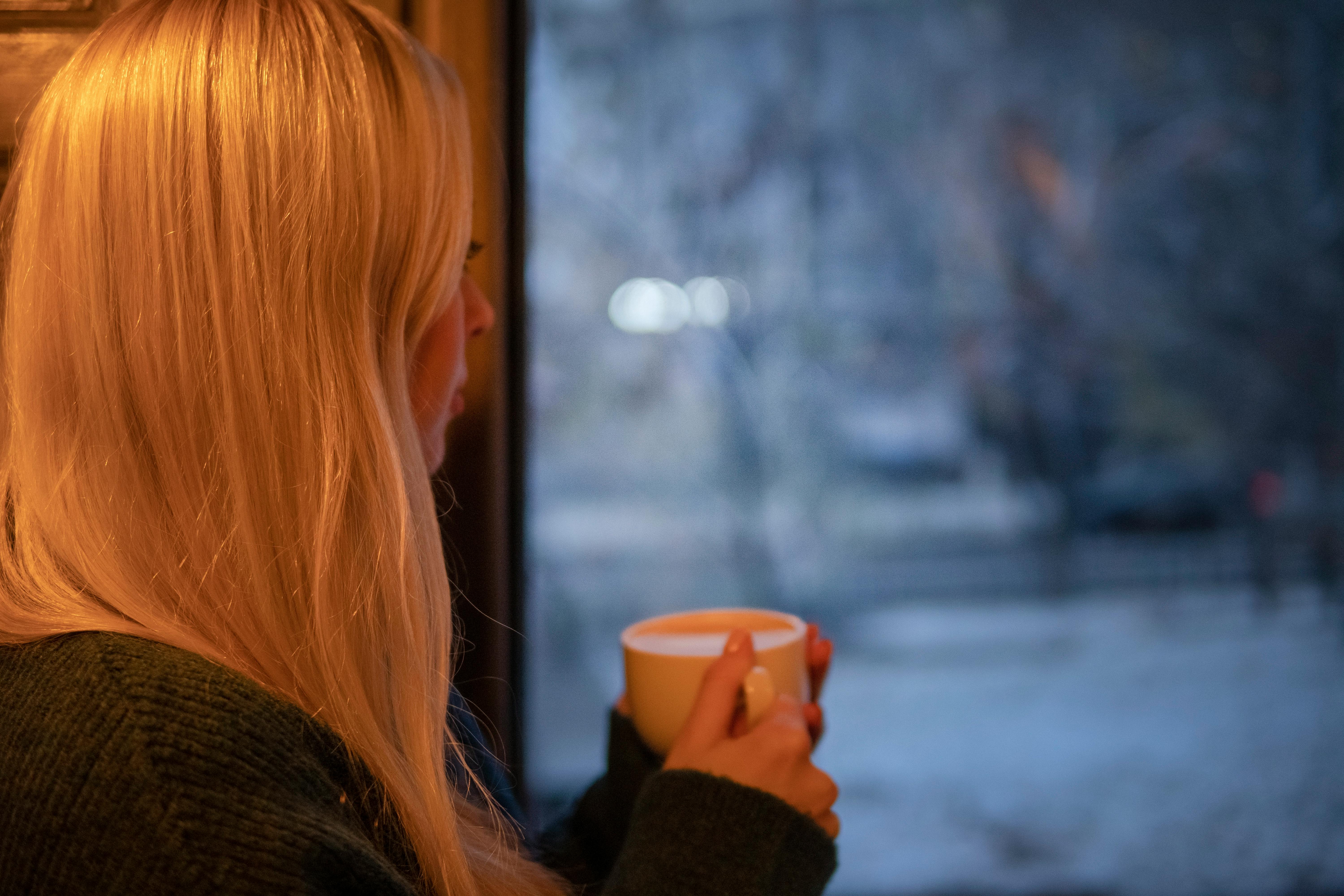 Ein Mädchen mit einer Kaffeetasse, das aus dem Fenster schaut | Quelle: Pexels