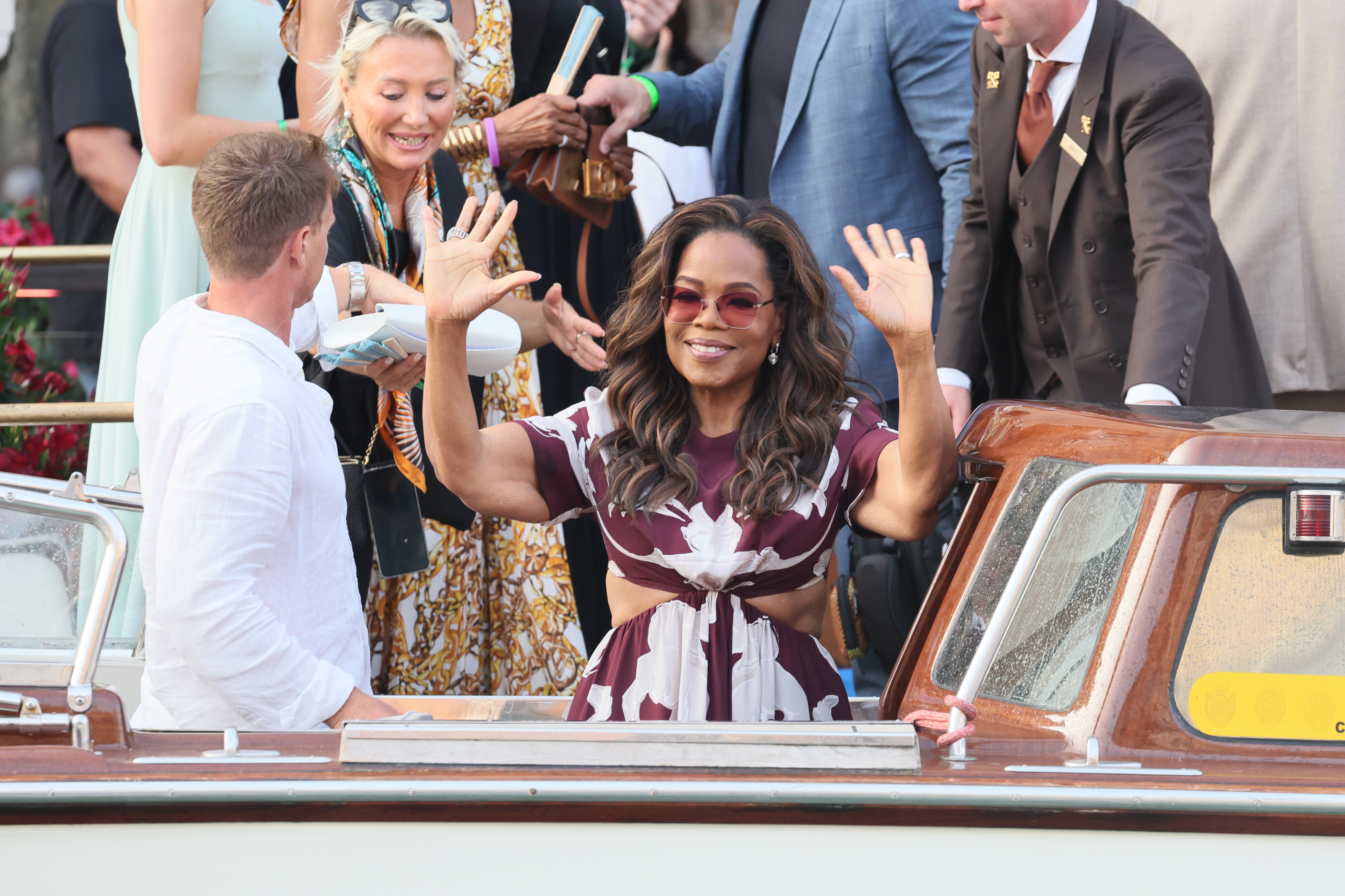 Oprah Winfrey lächelt und winkt der Menge zu, als sie vor der Hochzeit von Jeff Bezos und Lauren Sanchez in Venedig, Italien, am 26. Juni 2025 auf die Bühne tritt. Die lockere Haut um ihre Arme, die die Medien in Atem hält, ist sichtbar, als sie ihre Hände in die Luft hebt.