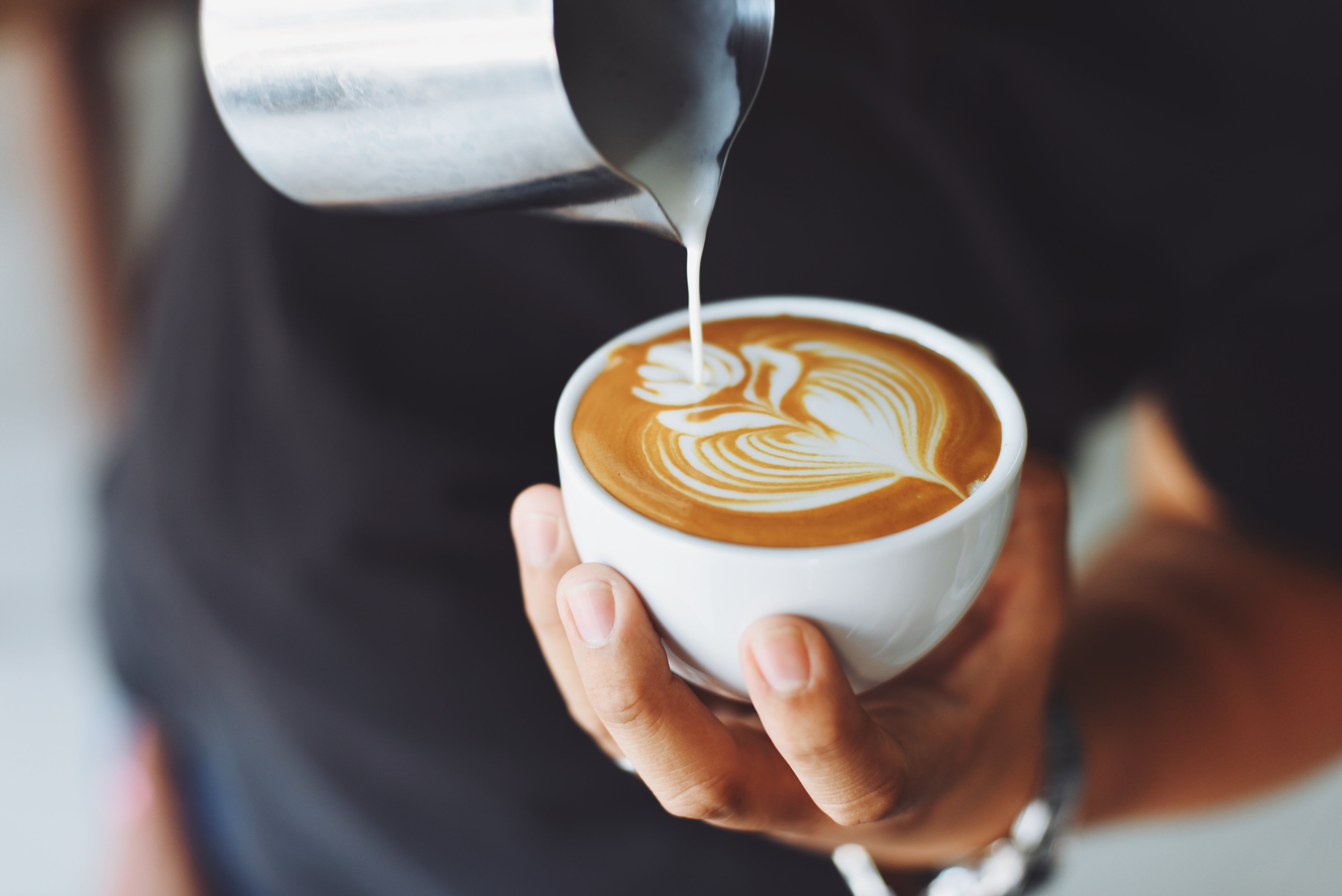 Eine Person hält eine Tasse Milchkaffee. | Quelle: Pexels
