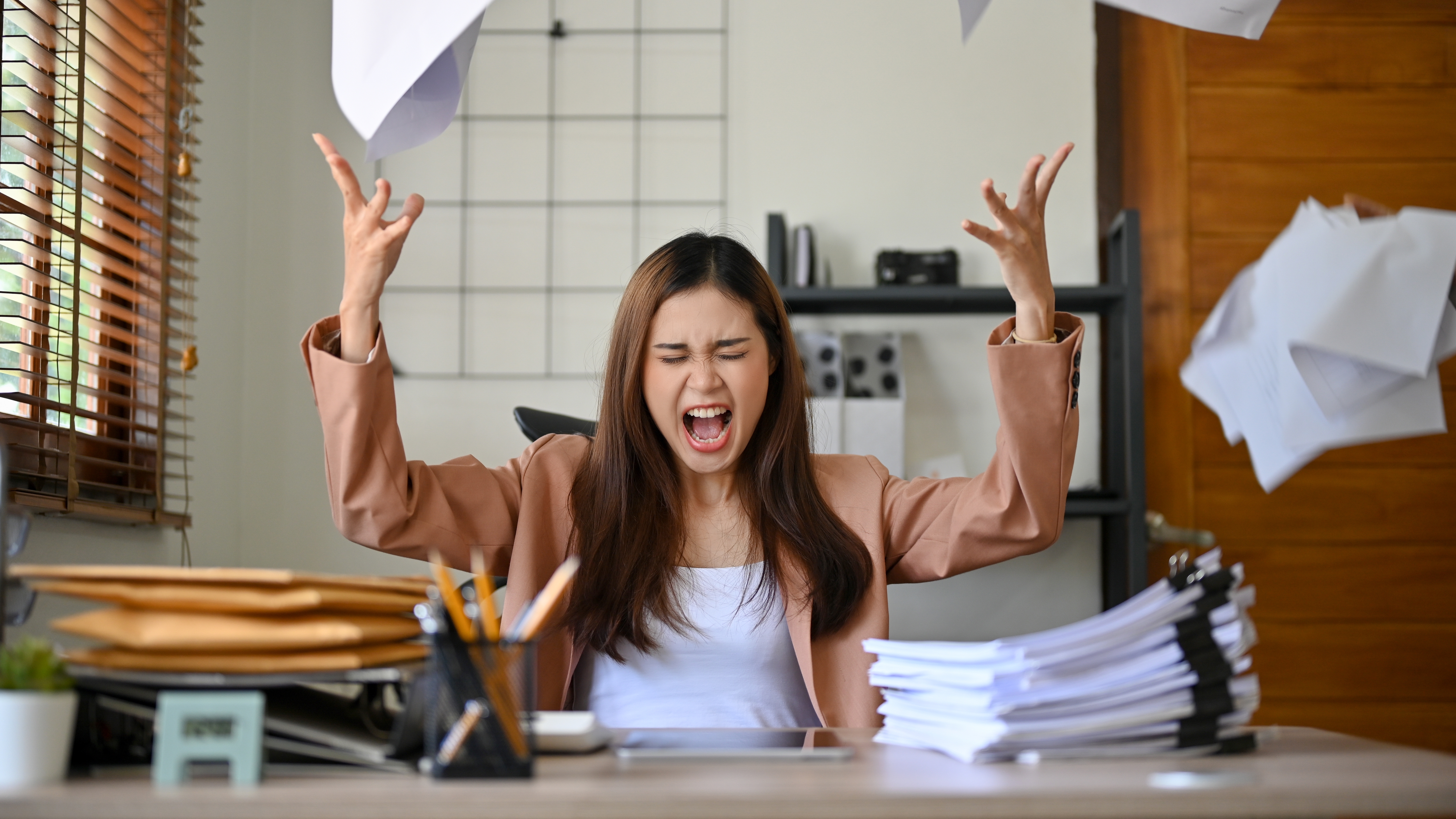 Eine Frau, die aus Wut Papiere in die Luft wirft.  | Quelle: Shutterstock/BongkarnGraphic