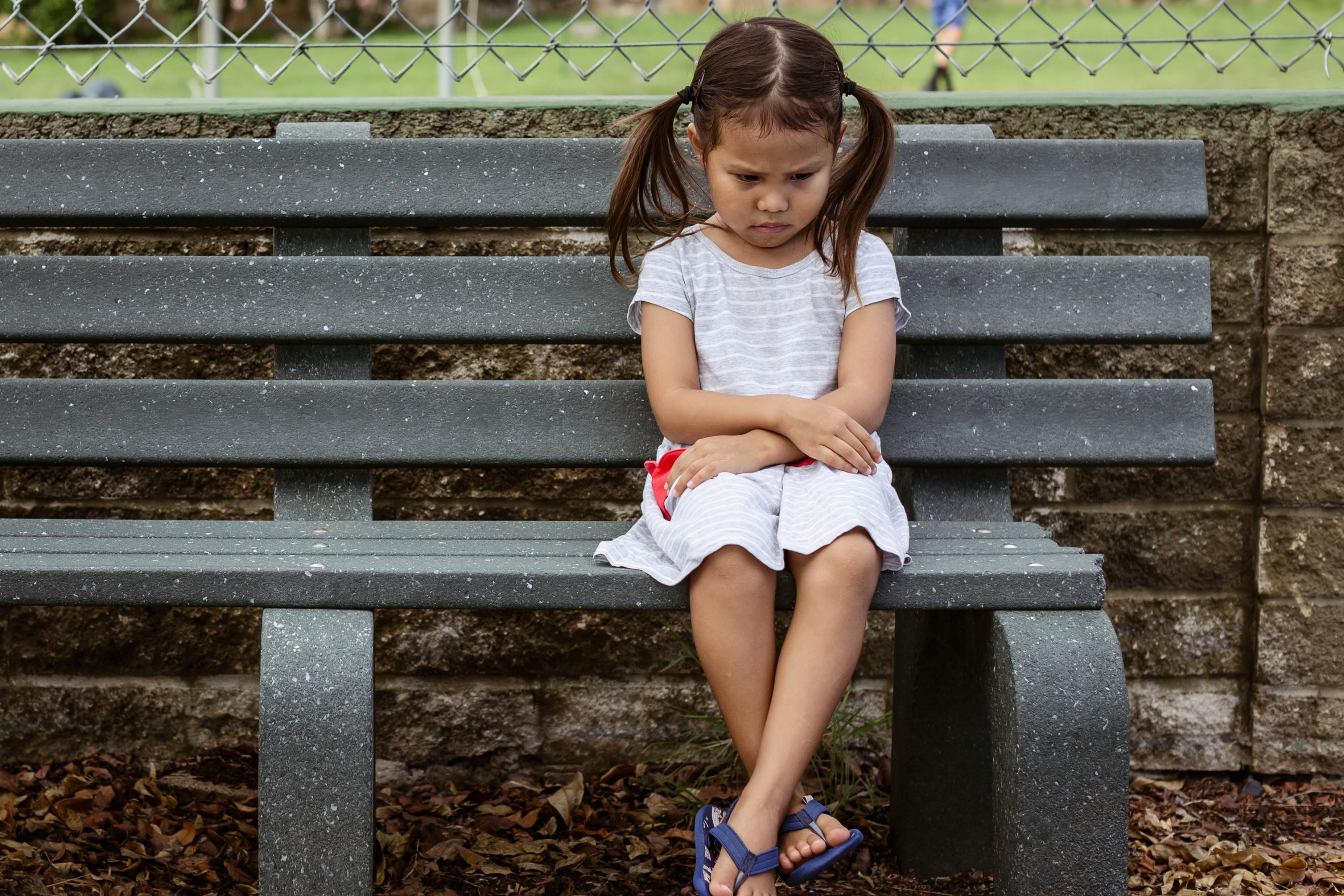 Ein unglückliches kleines Mädchen sitzt allein auf der Bank | Quelle: Shutterstock