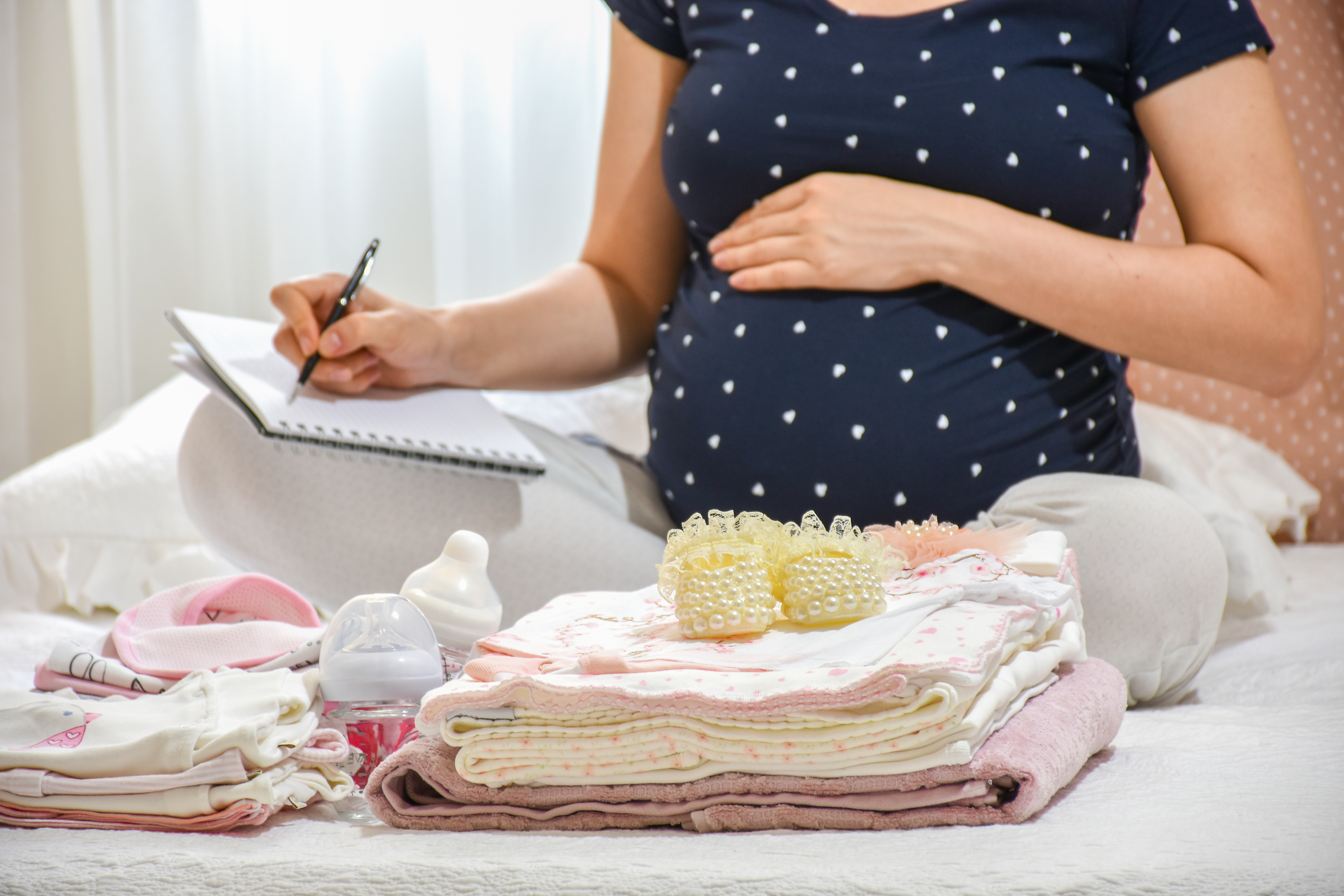 Eine schwangere Frau mit Babykleidung vor ihr | Quelle: Shutterstock