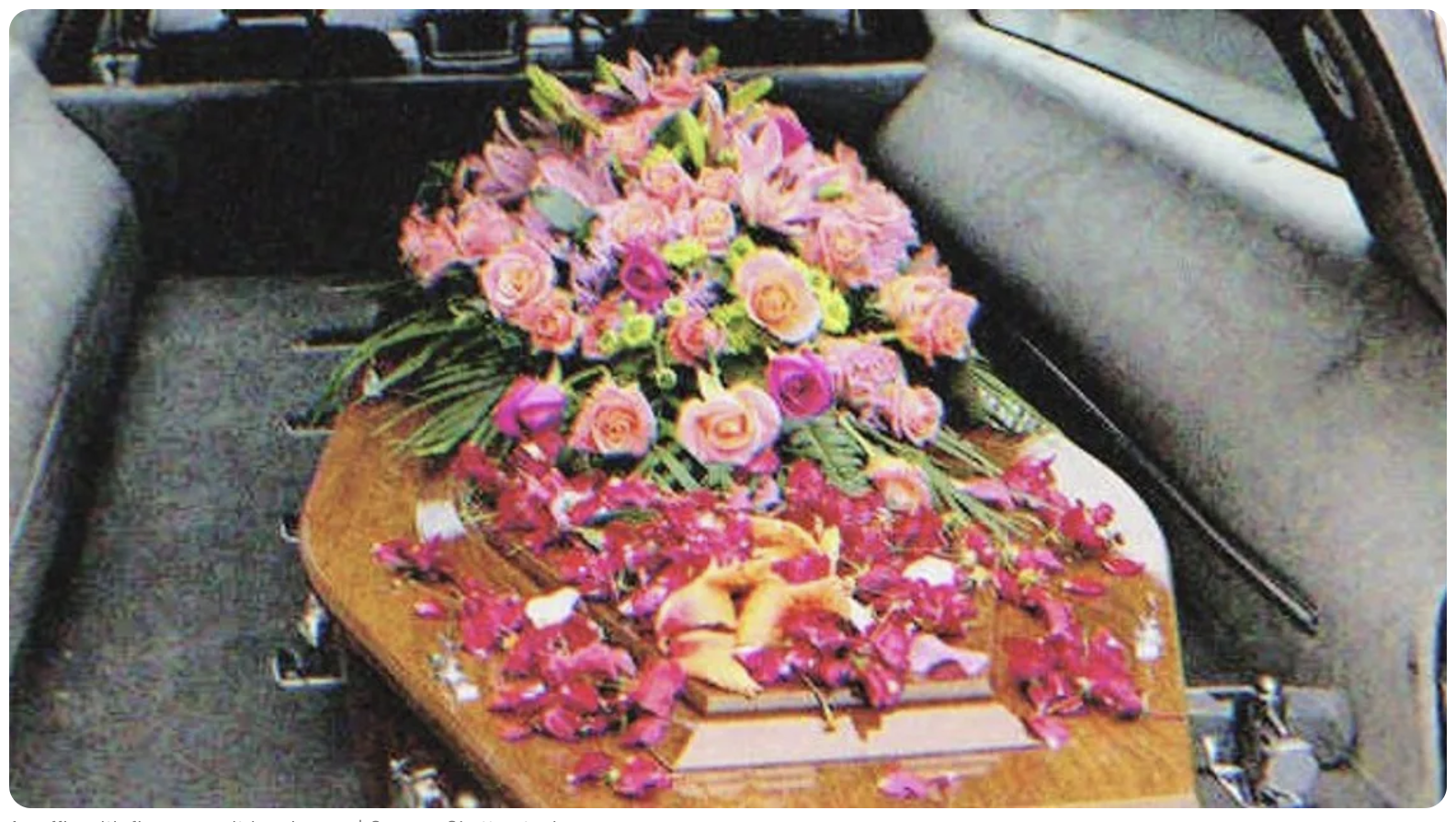 Ein Sarg mit Blumen darauf in einem Leichenwagen | Quelle: Shutterstock