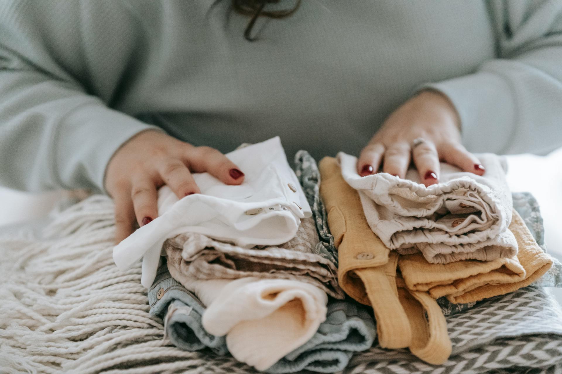 Eine Frau mit gefalteter Babykleidung | Quelle: Pexels