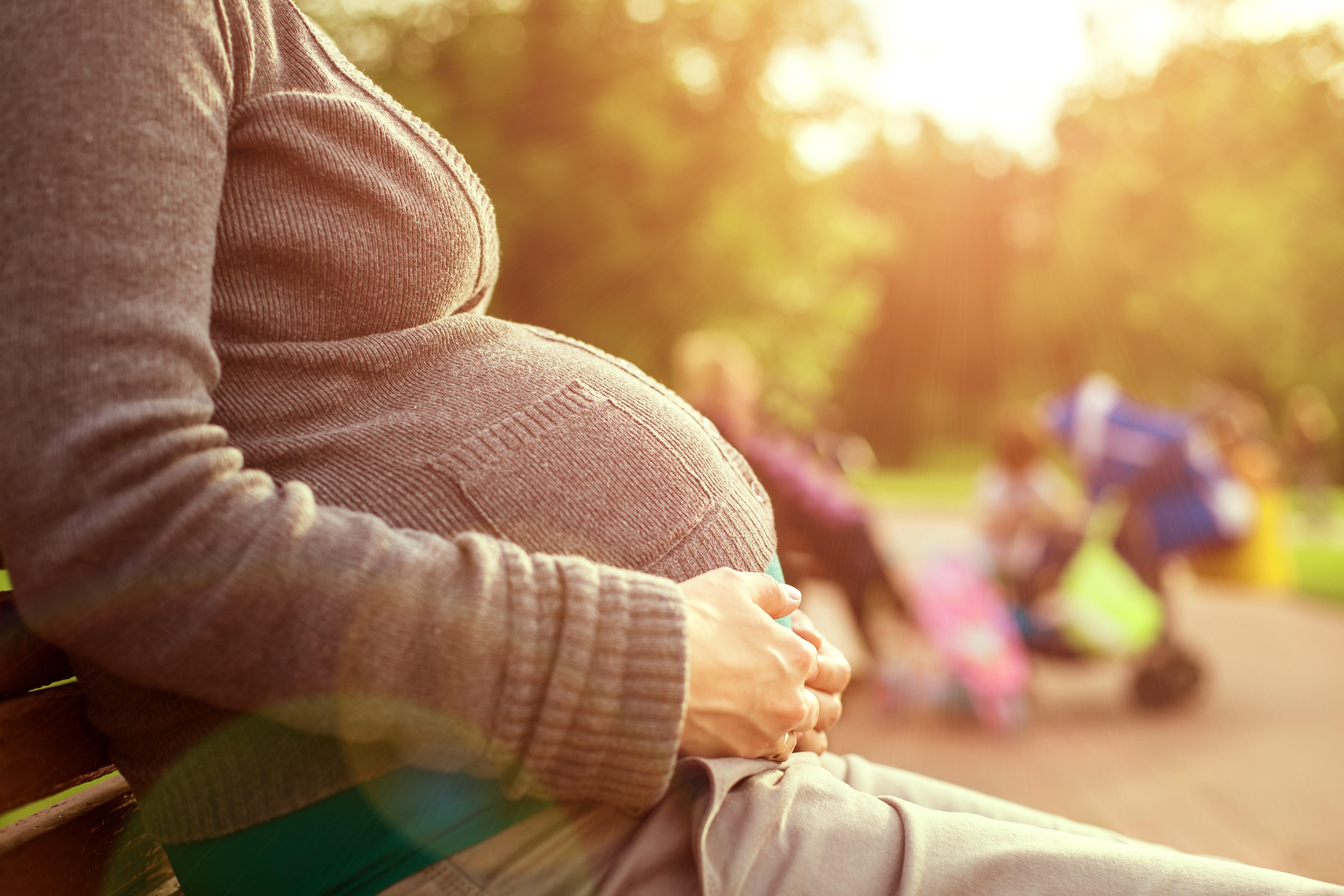 Schwangere Frau sitzt auf einer Bank, im Hintergrund spielen die Kinder | Quelle: Shutterstock