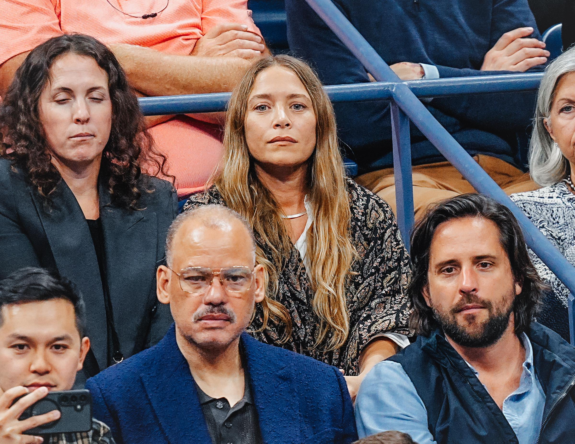 Umrahmt von langem, wallendem, welligem blond-braunem Haar mit Mittelscheitel, zeigte die 39-jährige Mary-Kate Olsen am 3. September 2025 auf der Zuschauertribüne der US Open einen ruhigen, gelassenen Gesichtsausdruck mit dezentem Make-up und einer zarten silbernen Halskette, während sie eine dunkel gemusterte, handgefertigte Jacke über einem hellen Oberteil trug.