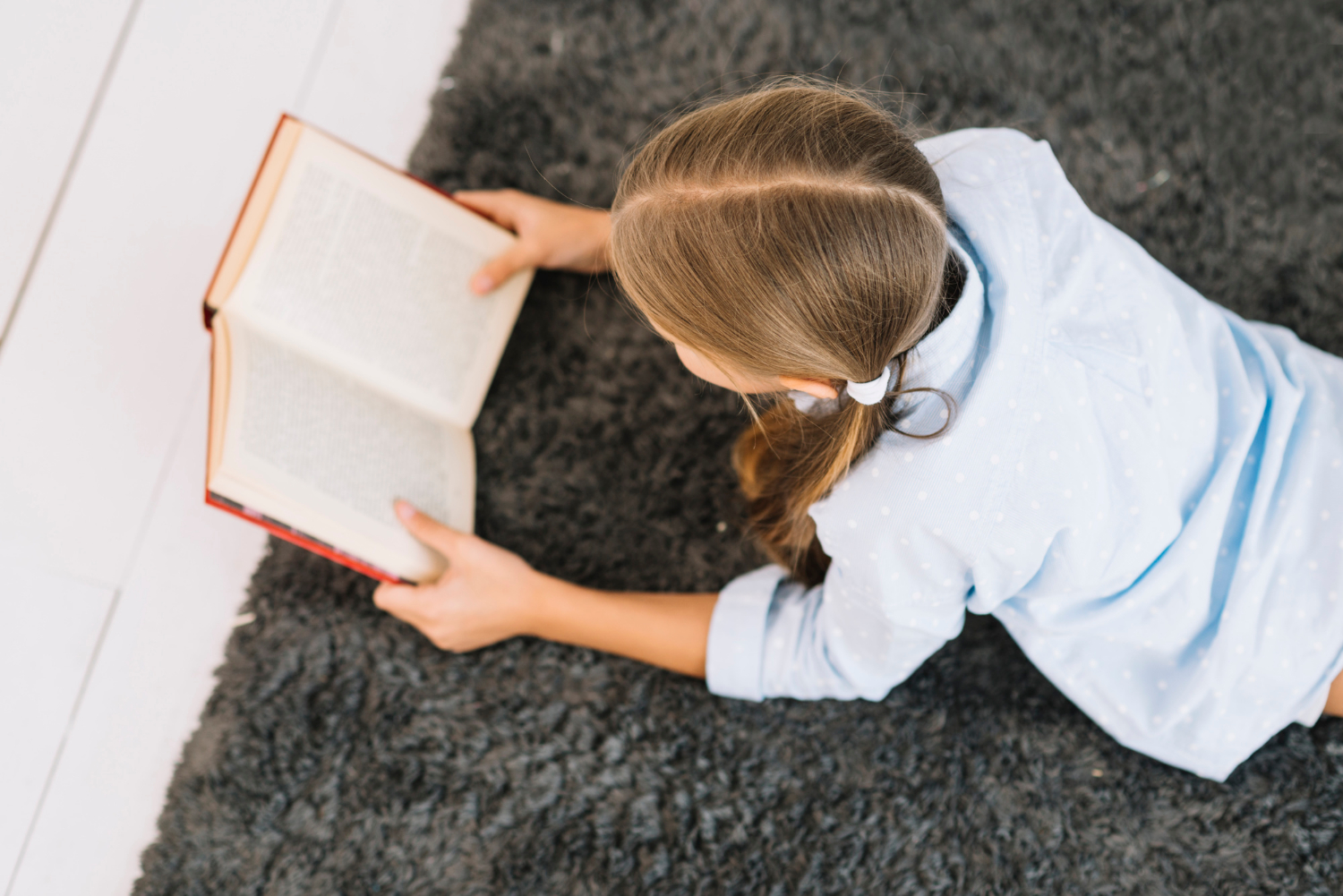 Ein Mädchen liegt auf einem Teppich und liest ein Buch | Quelle: Freepik